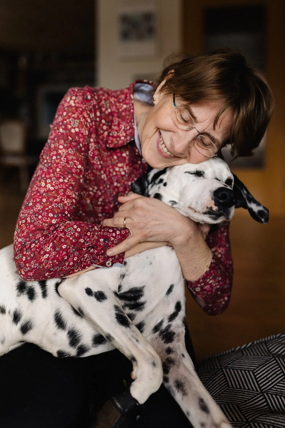 Frau umarmt und kuschelt einen Dalmatiner-Hund, beide haben ein glückliches Lächeln und wirken zufrieden.