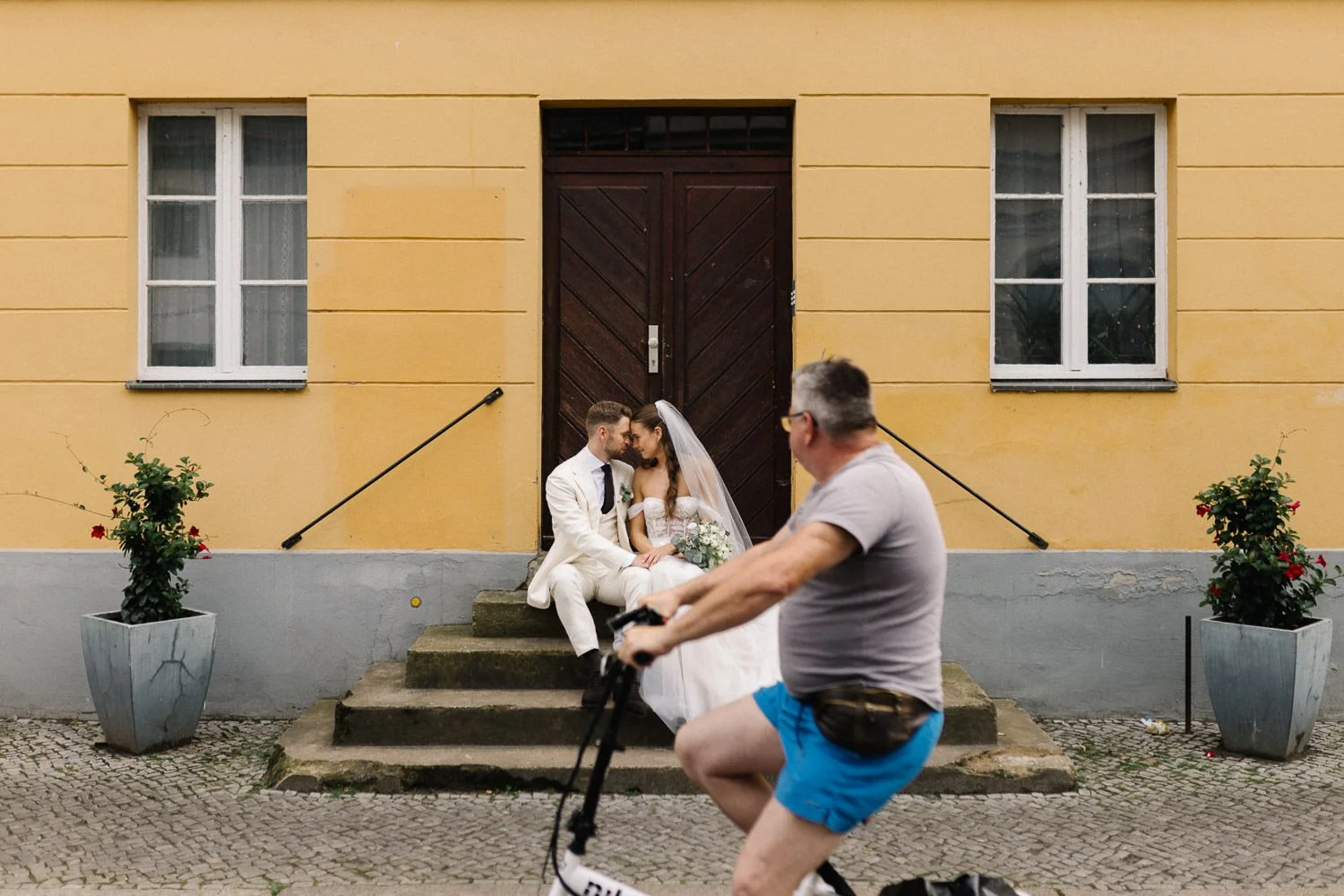 Brautpaar sitzt auf Treppe, Fahrrad fährt im Vordergrund vorbei