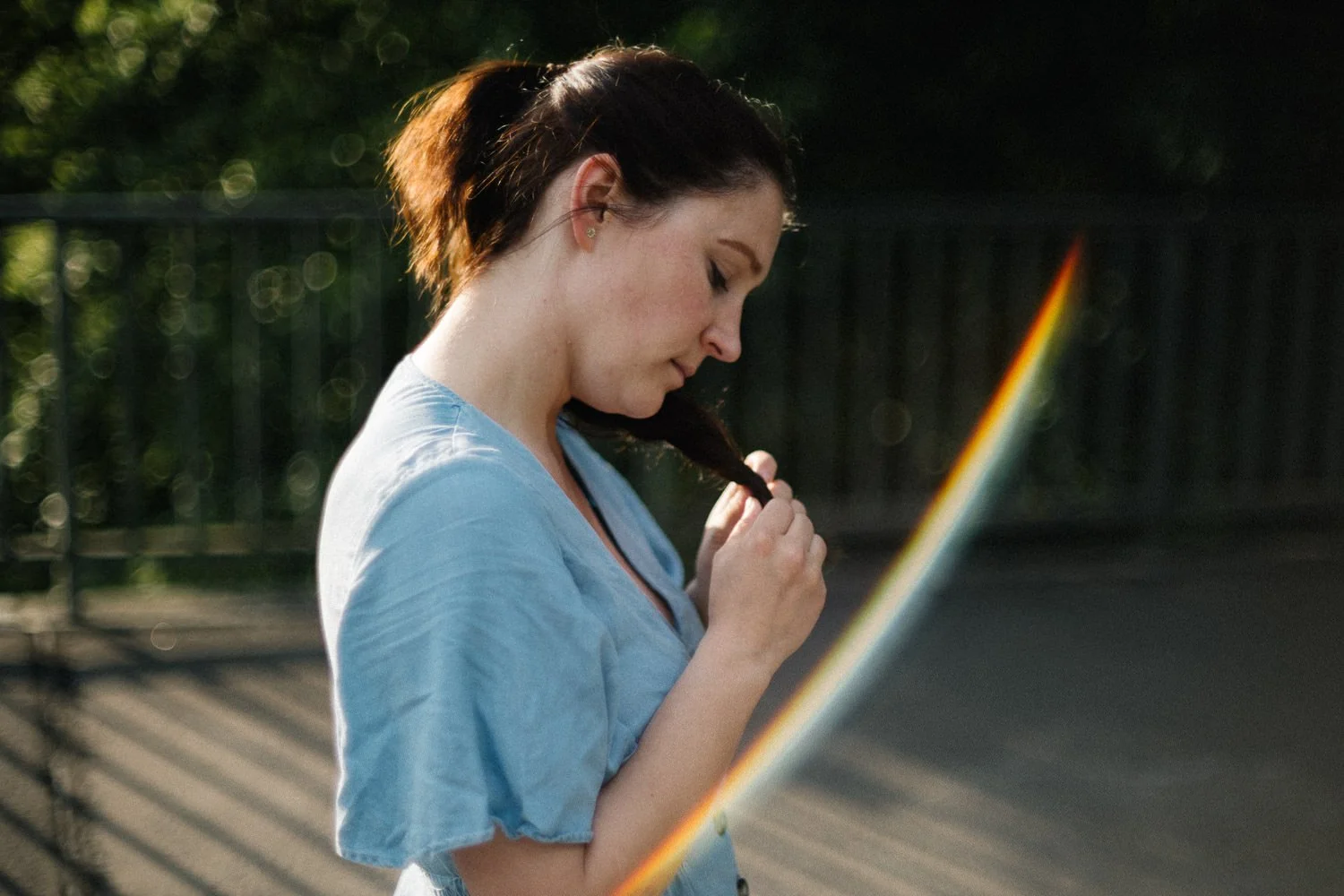 Eine Frau mit braunem Haar in einem Pferdeschwanz, die an einem sonnigen Tag liest oder schaut, während sie einen seitlichen Blick nach unten hat, im Freien mit einem Zaun im Hintergrund.
