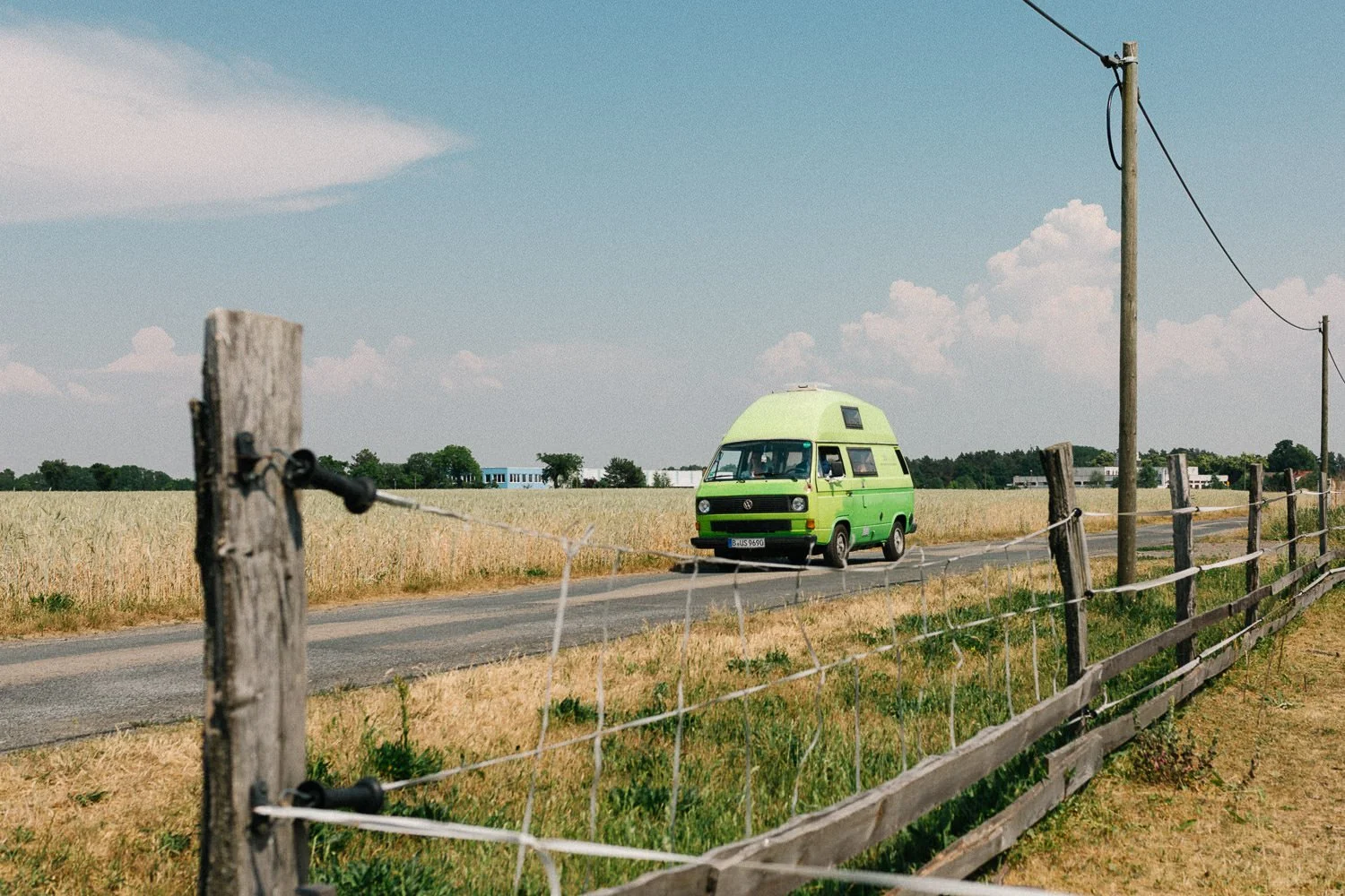 Grüner VW T3 Bulli fährt Feldweg entlang, Sommer, blauer Himmel