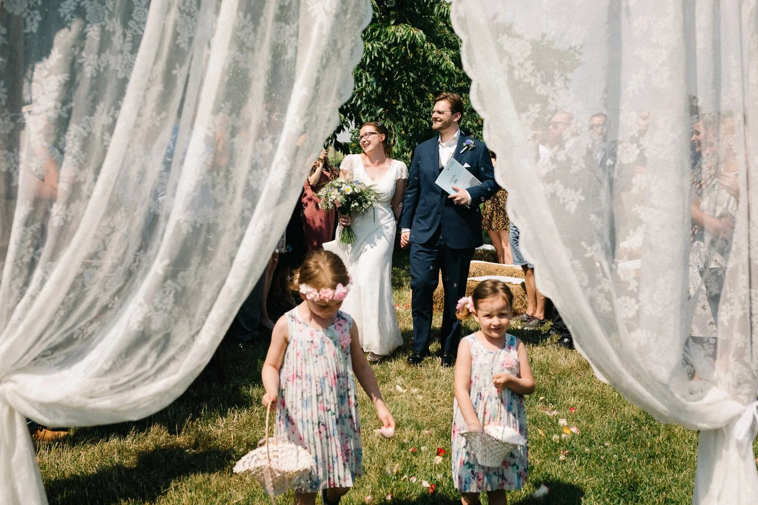 Blick durch Traubogen, Blumenkinder im Vordergrund, Brautpaar im Hintergrund