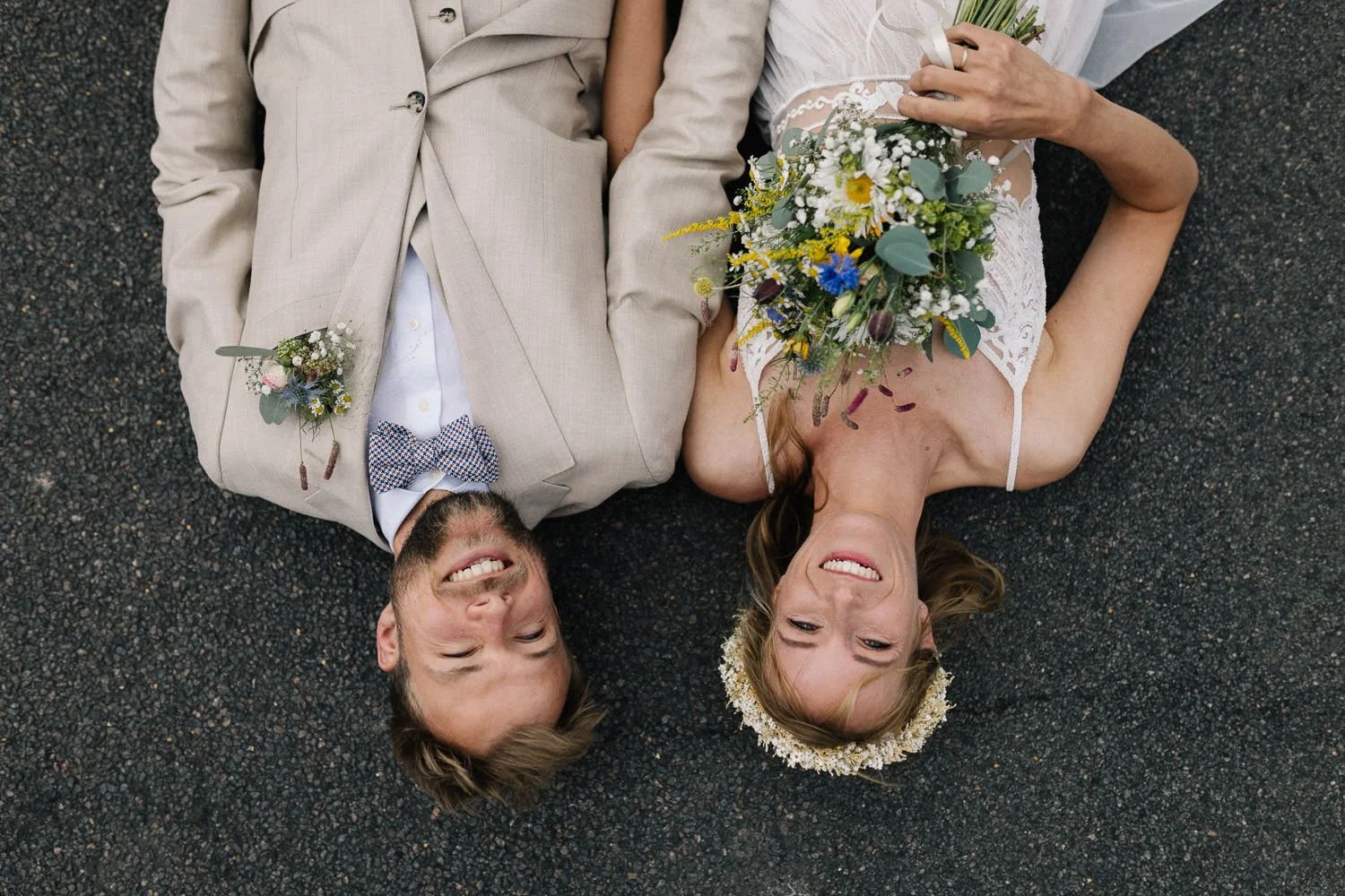 Lachendes Brautpaar liegt auf einer Straße kreatives Hochzeitsfoto