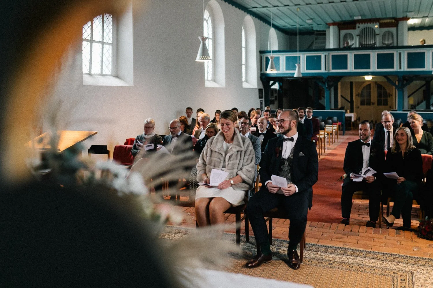 Brautpaar während Trauung, sitzend, Hochzeitsgesellschaft Hintergrund