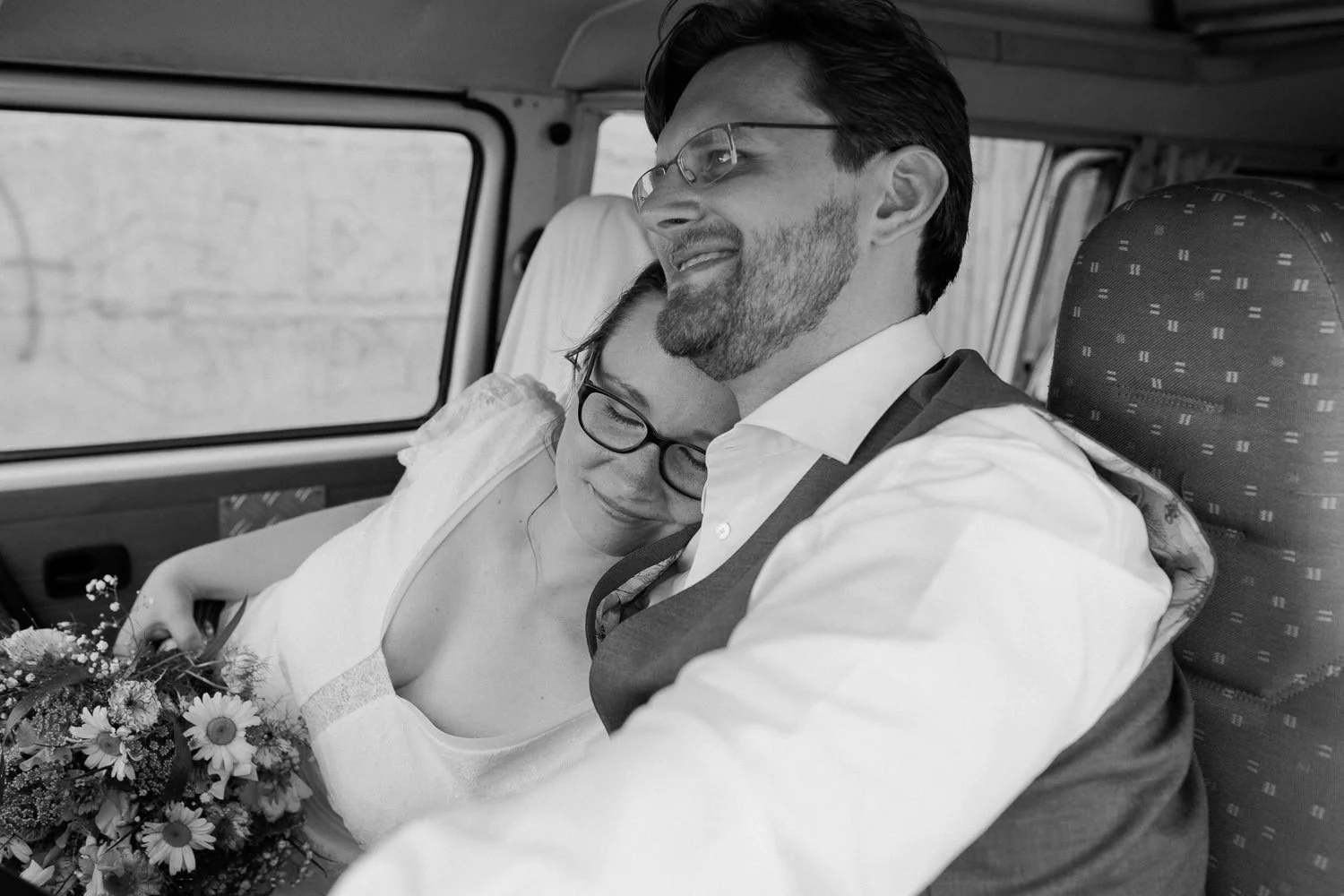 Brautpaar sitzt in Auto, Braut legt Kopf an Schulter von Bräutigam, Schwarz-weiß Foto
