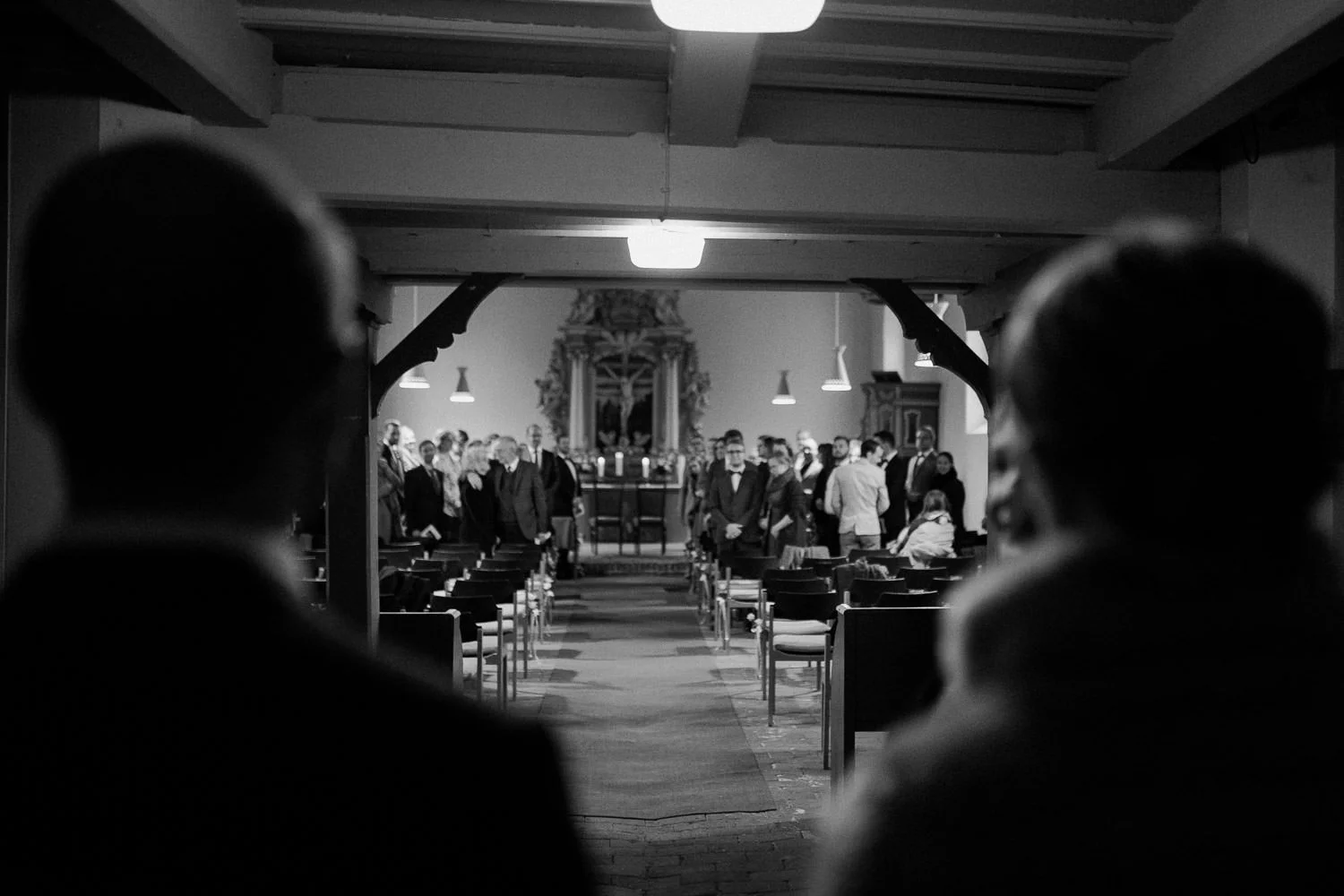 Brautpaar betritt Kirche, Blick von hinten über die Schultern, Gäste stehen auf, Schwarz-weiß Foto