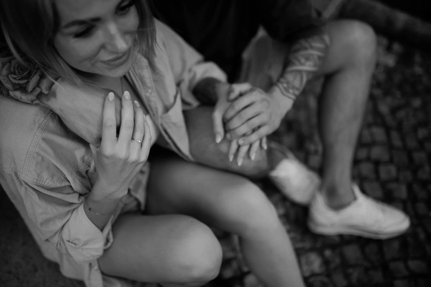 Schwarz-weiß-Foto von einem Mann, der einer Frau auf ihren Bauch tätschelt, während sie lächelt, beide sitzen auf einer gepflasterten Oberfläche, Nahaufnahme.