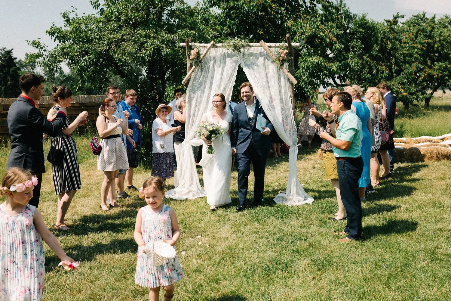 Brautpaar läuft durch Traubogen, Hochzeitsgäste klatschen rechts und links, Vierseithof Familie List