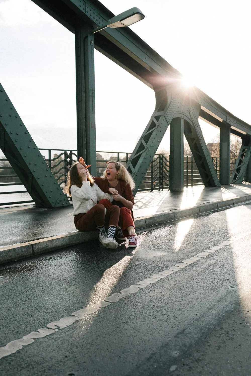 Zwei lachende Mädchen Schwestern sitzen auf dem Boden auf der Glienicker Brücke in Potsdam und haben Spaß miteinander.