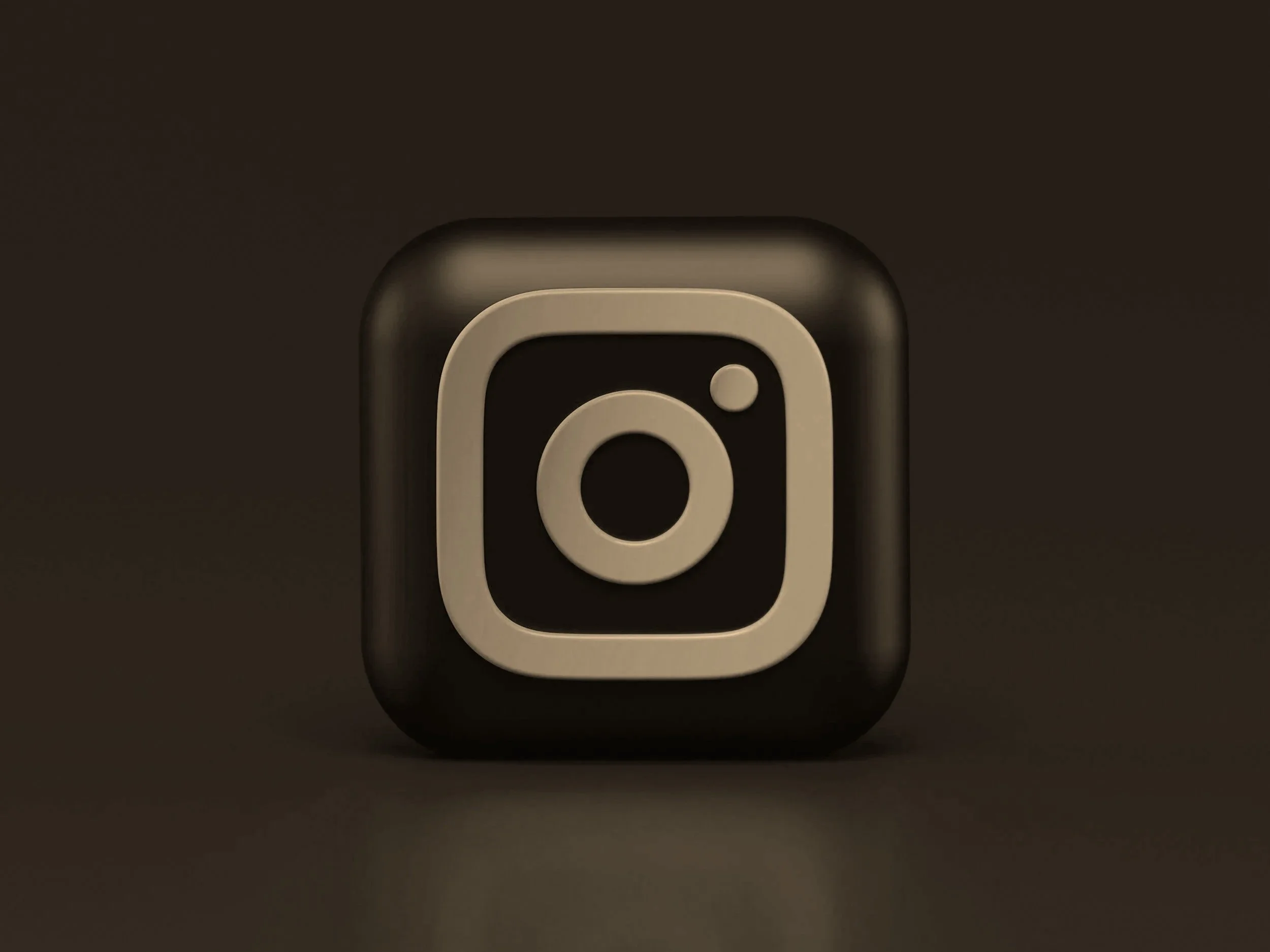 Close-up of a black 3D Instagram logo icon with a white outline on a dark background.