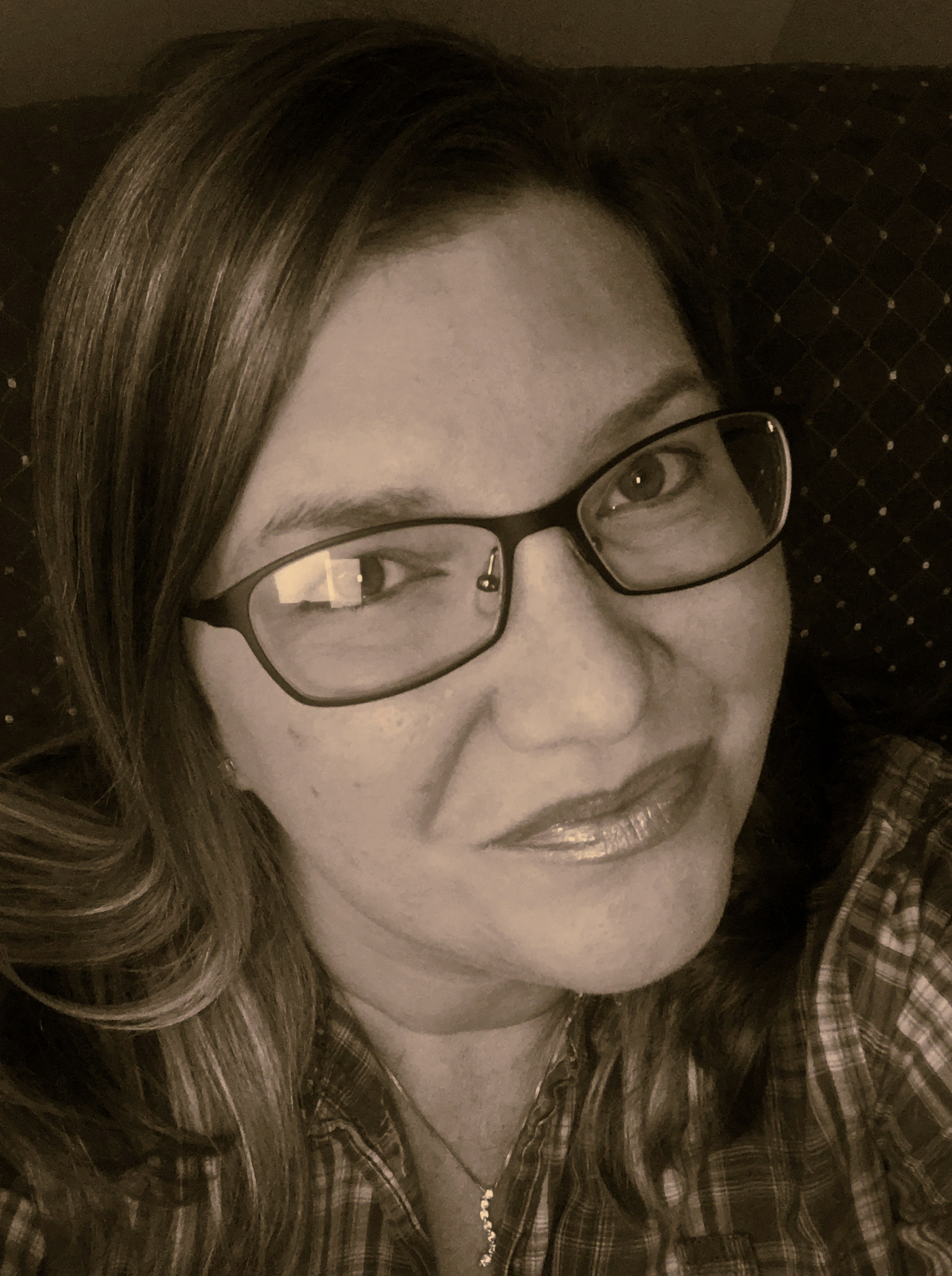 A woman with long hair, wearing glasses and a plaid shirt, smiling at the camera.