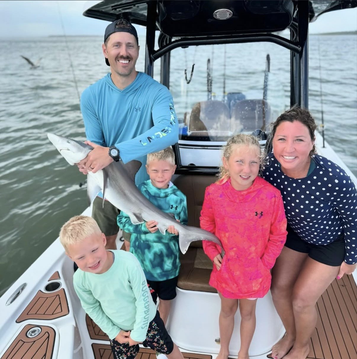 A family on a boat holding a small shark they caught, smiling and enjoying a day of fishing on the water.