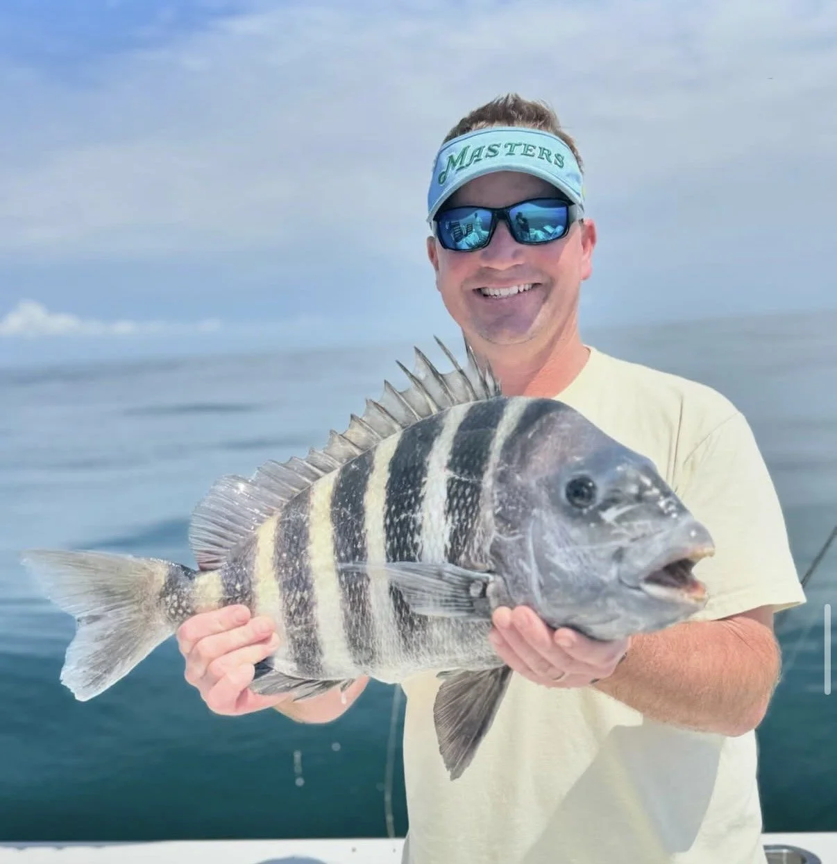 A man on a boat holding a large fish with black and white vertical stripes in front of a calm ocean and cloudy sky.