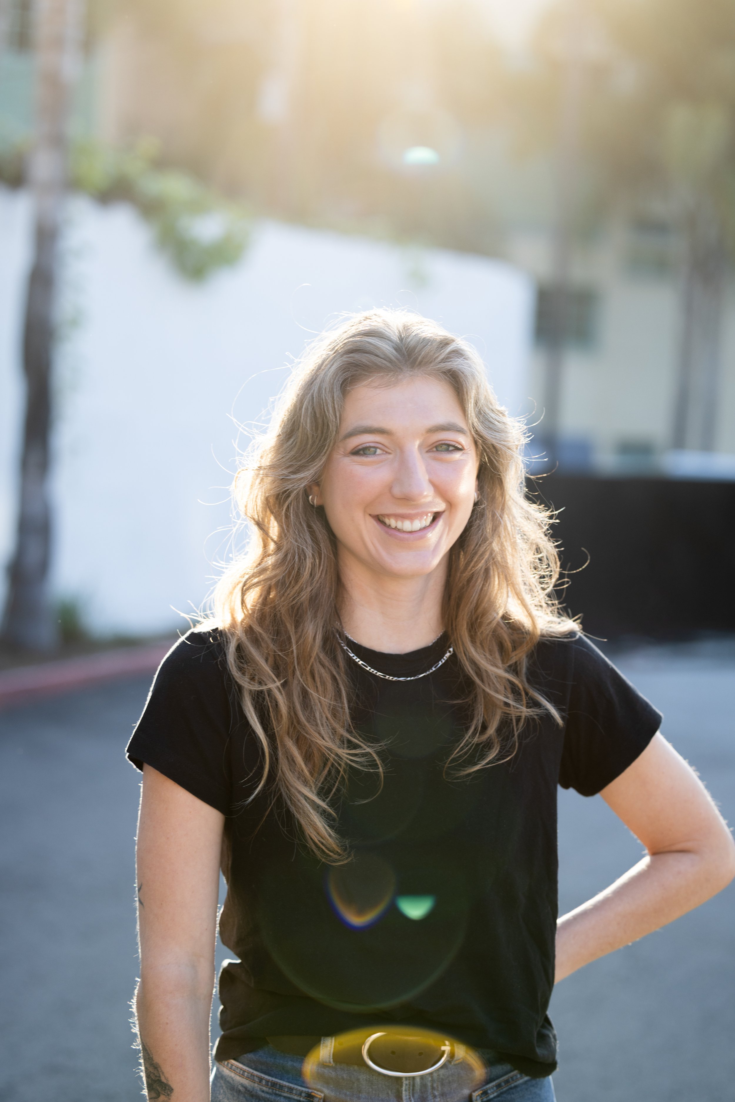 A woman with wavy blonde hair smiling outdoors on a sunny day. Year After Year Media.  Mini-Documentary.  Non-Profit.  Organization.  Film production.