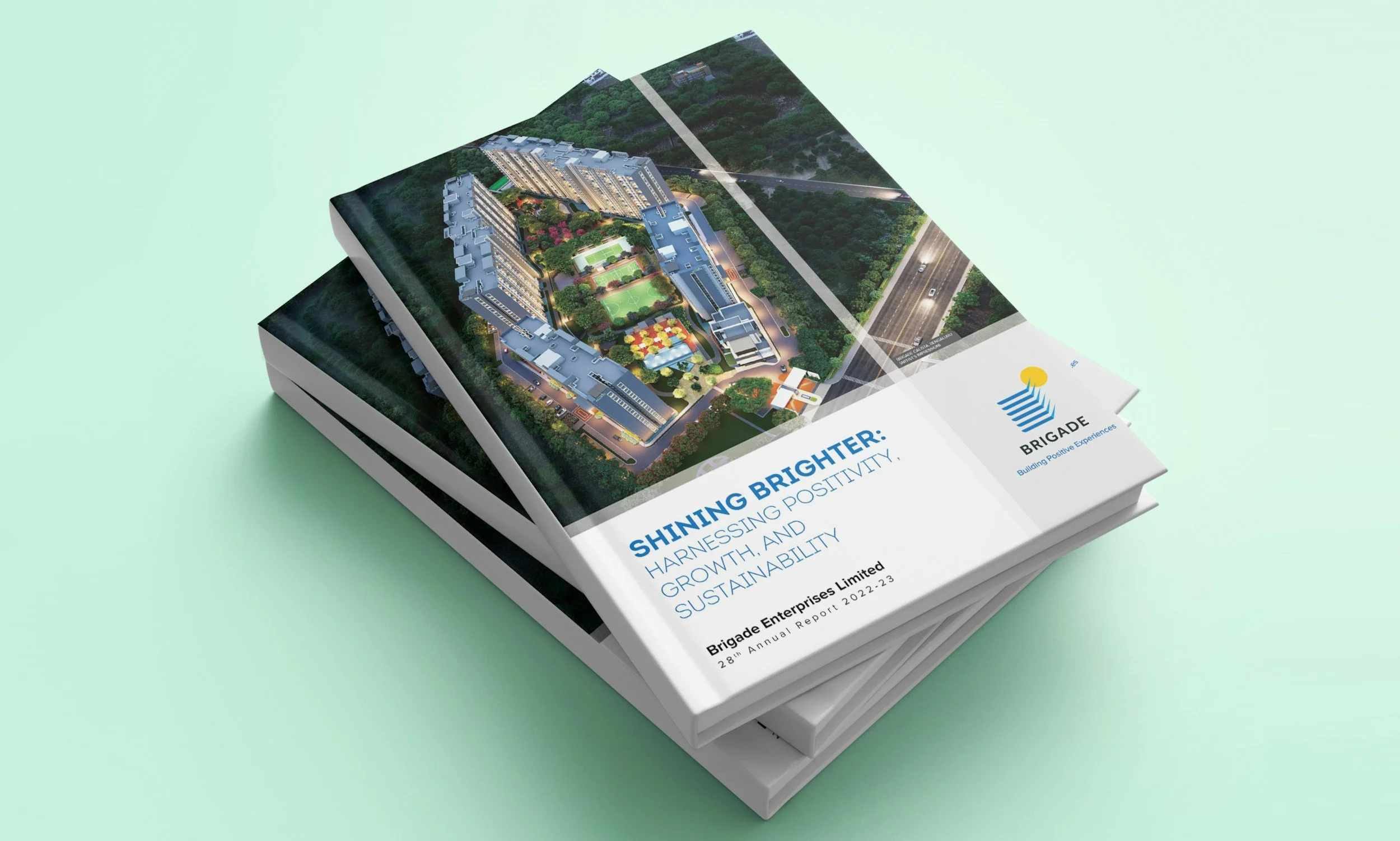 Cover of Brigades annual report featuring an aerial 3D rendering of a residential complex with buildings, green spaces, and a swimming pool, with the headline 'Shining Brighter: Harnessing Positivity, Growth, and Sustainability.'