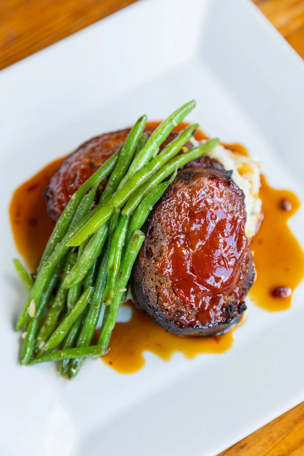 Meatloaf topped with tomato sauce, served with green beans on a white plate.