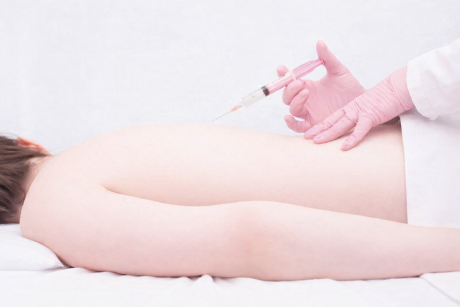 A person receiving a vaccination injection in their upper arm by a healthcare professional wearing pink gloves.