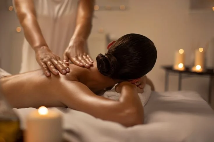 A woman receives a back massage in a spa setting with candlelight in the background.