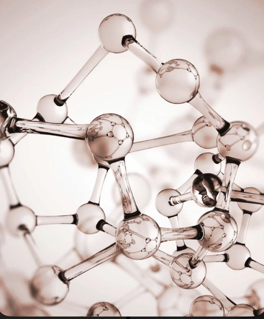 Close-up of a model representing a molecular structure with interconnected transparent spheres and sticks, reflecting light with a rose gold tint.