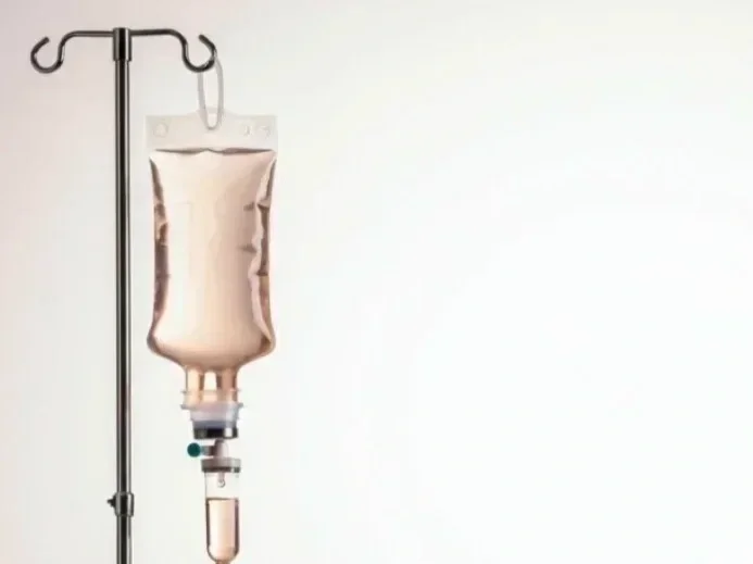 A IV drip bag hanging on a stand against a plain white wall.
