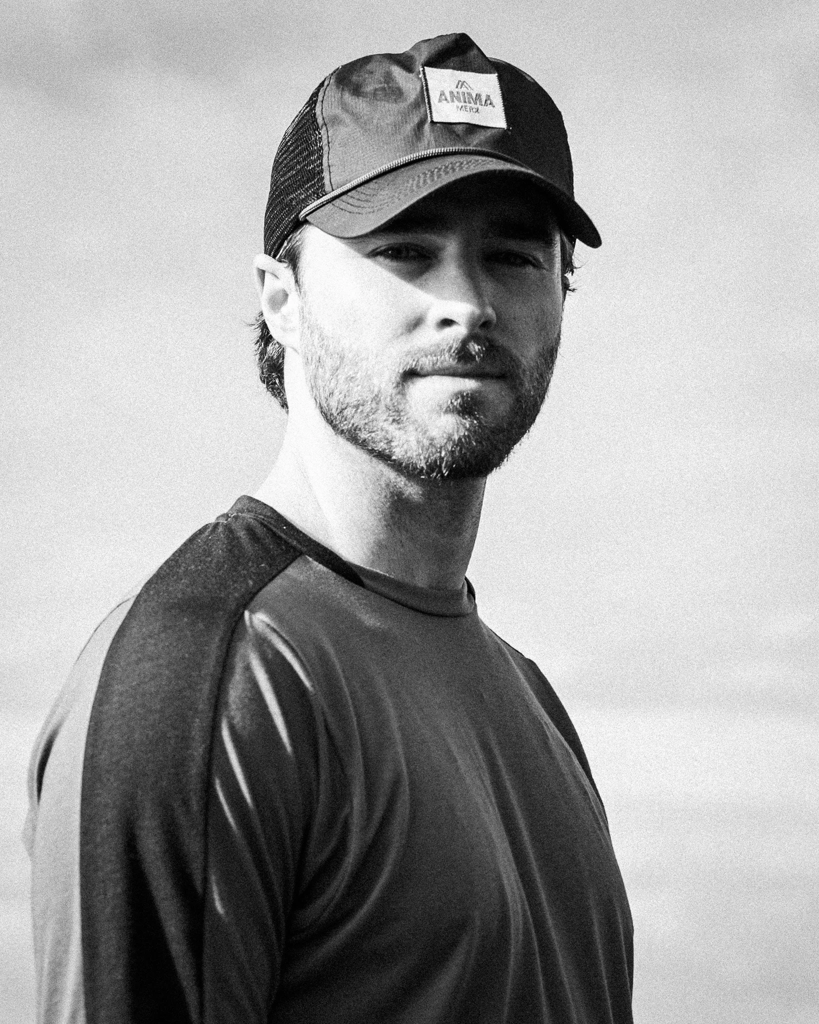 Black and white photo of a young man wearing a baseball cap and athletic shirt, looking at the camera with a slight smile.