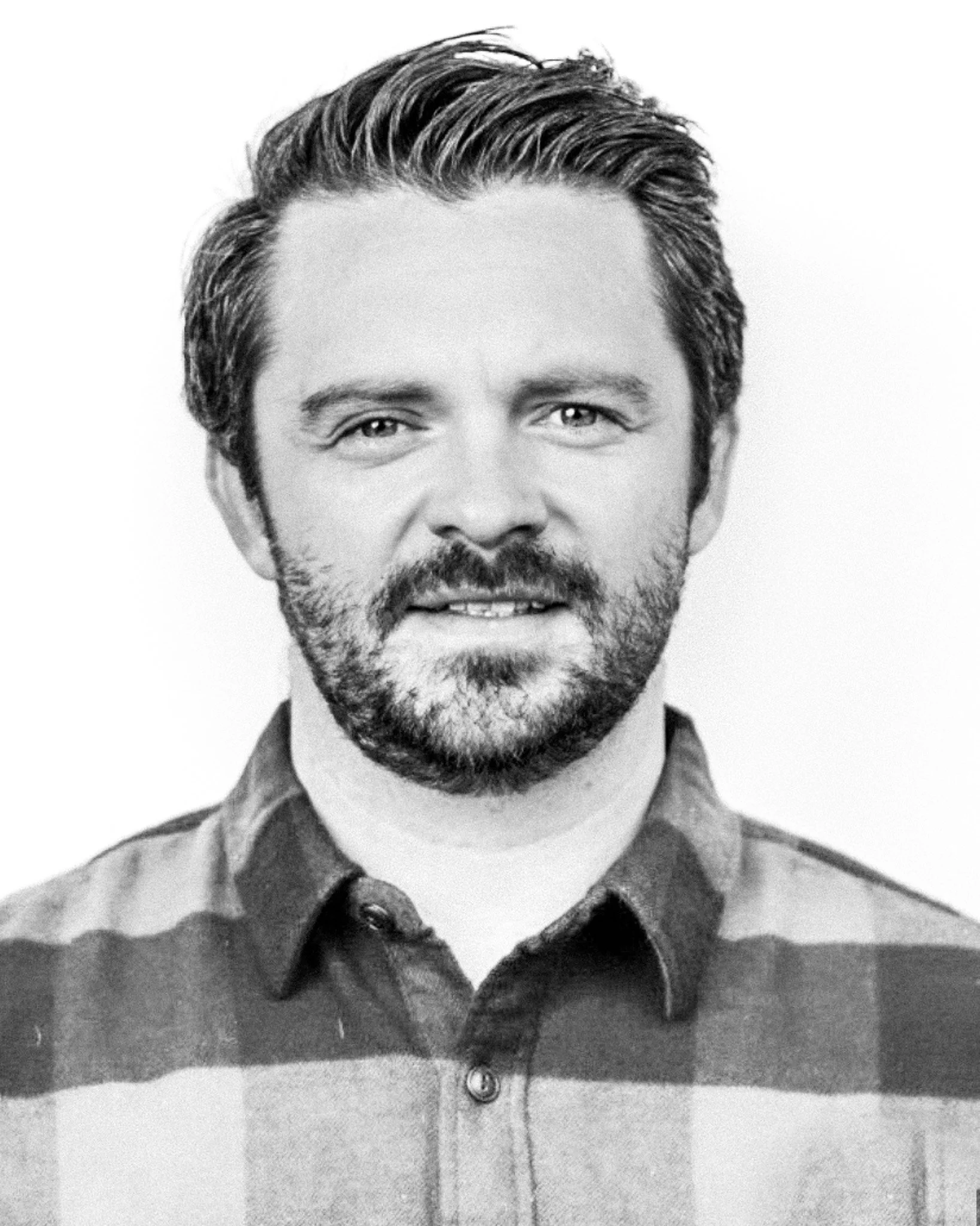 Black and white portrait of a man with styled hair, a beard, and wearing a plaid shirt.