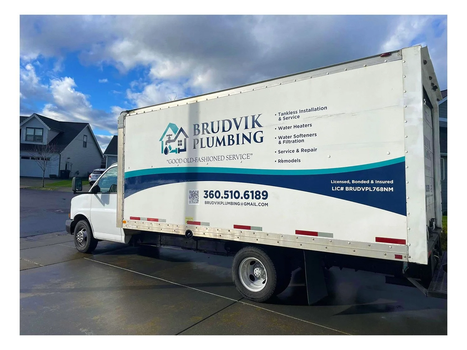 Brudvik Plumbing truck parked on a driveway under a partly cloudy sky, with houses visible in the background.
