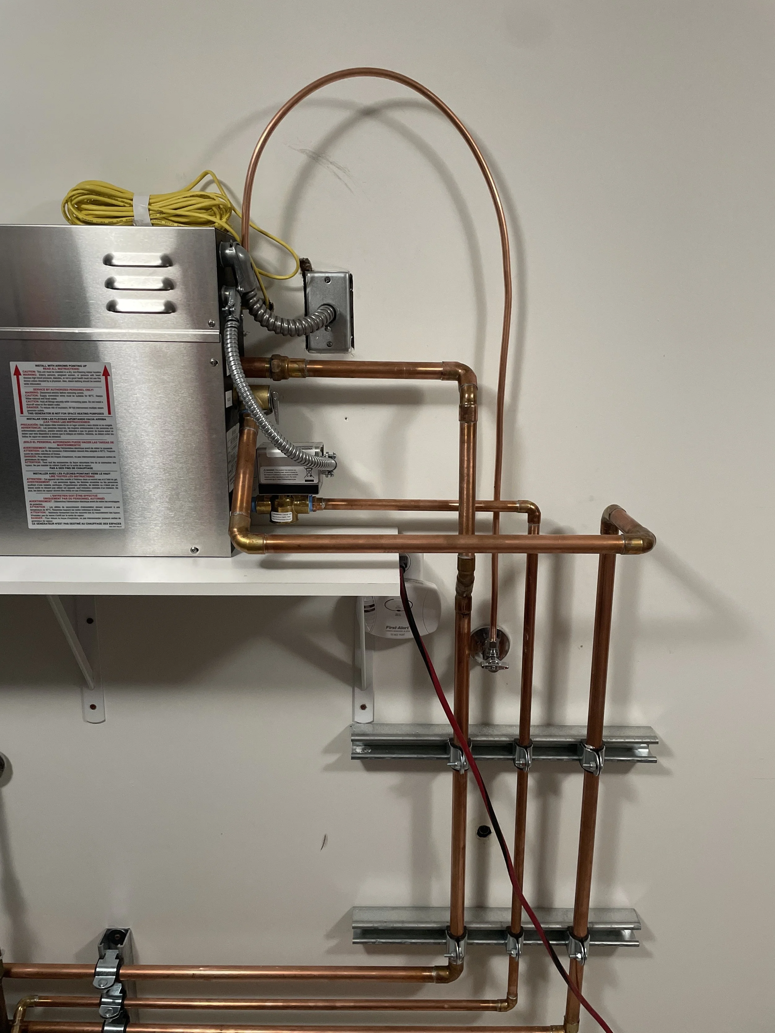 Copper plumbing pipes connected to a silver metal boiler on a white wall.