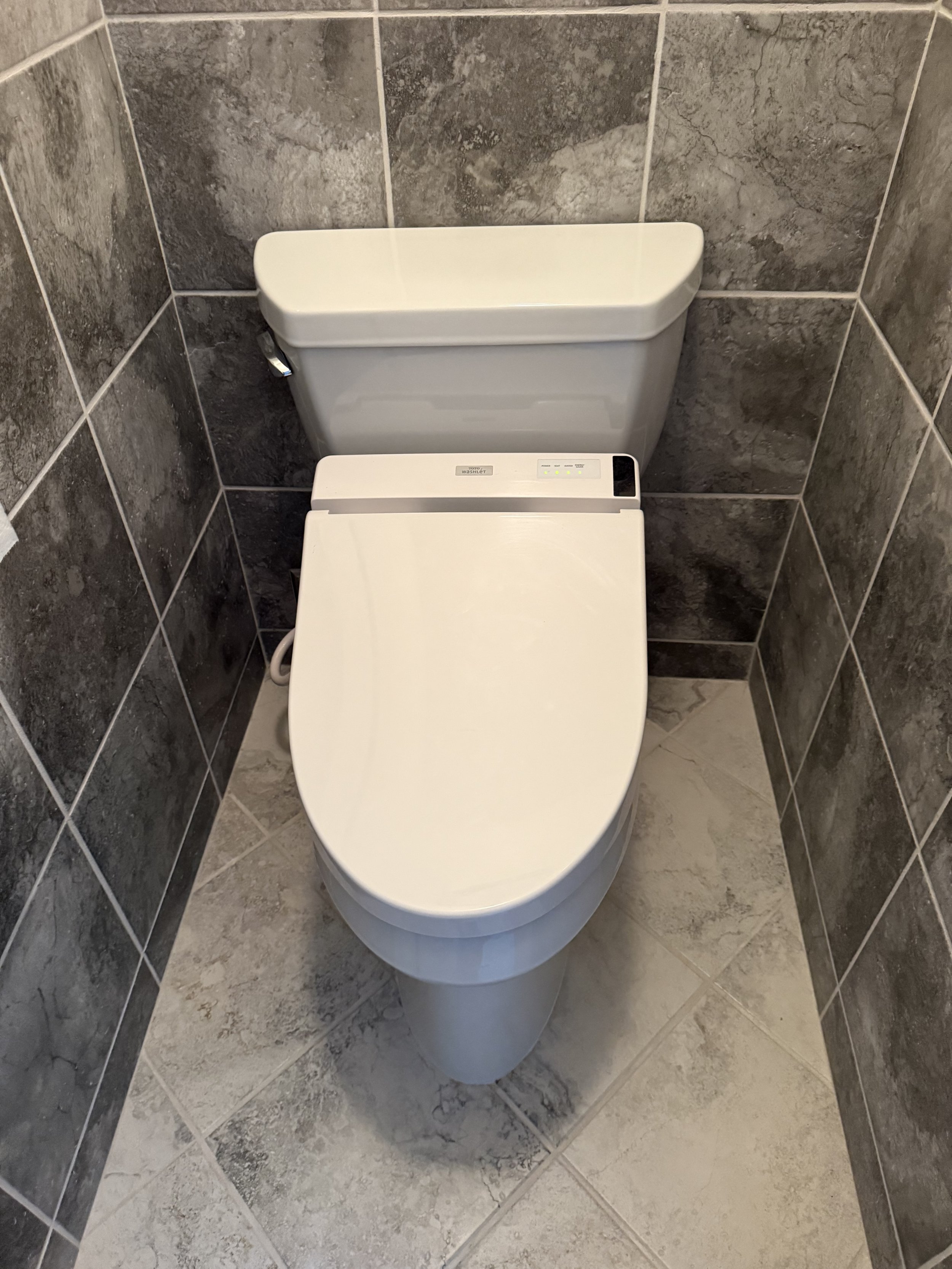 A modern toilet with a bidet seat in a small tiled bathroom.