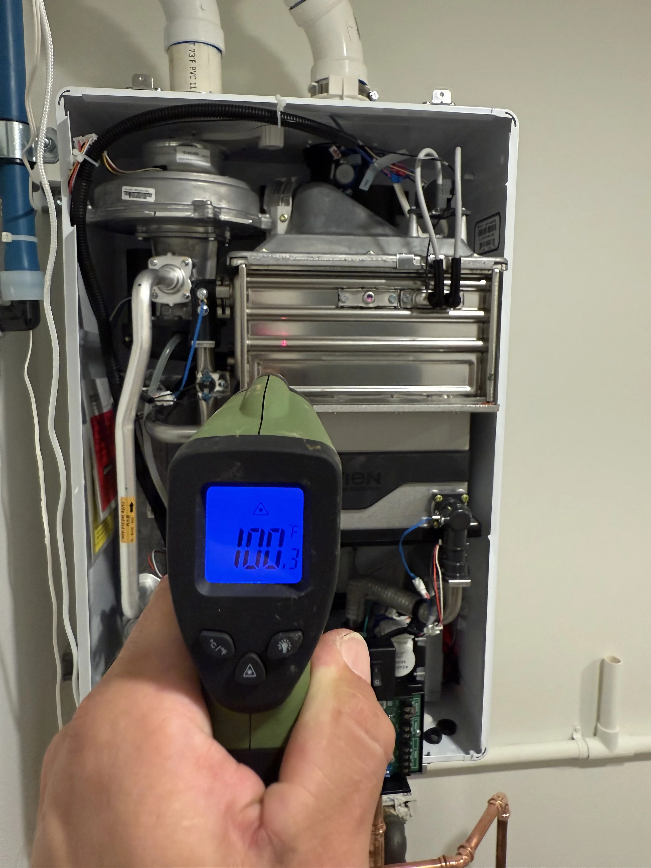 A technician is measuring the temperature of an industrial boiler with a handheld infrared thermometer, showing 100.5°F.
