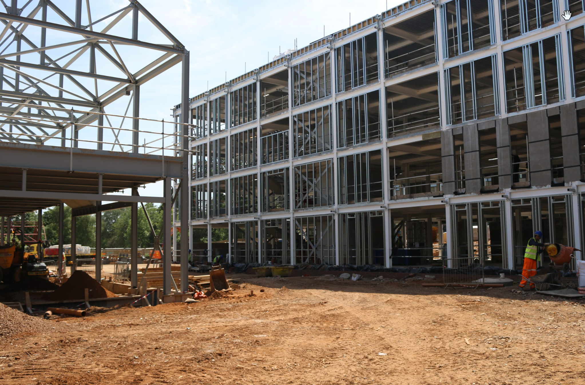 Modern house with wooden exterior, large windows, and stone stairs, set against a background of rolling green hills and snow-capped mountains.