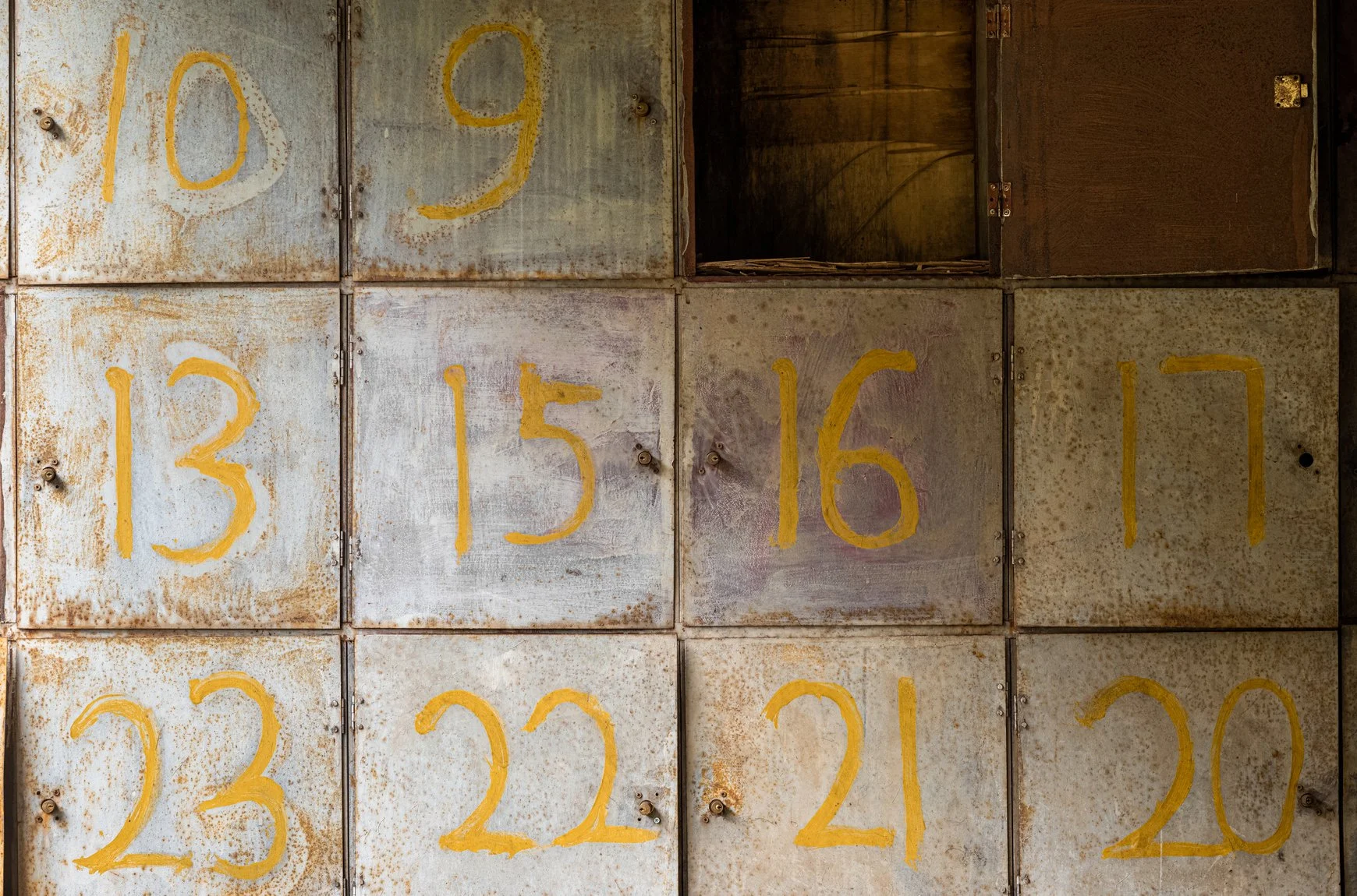 Rusty metal boxes with yellow numbers painted on them, arranged in a grid. The numbers include 10, 9, 13, 15, 16, 17, 23, 22, 21, and 20.