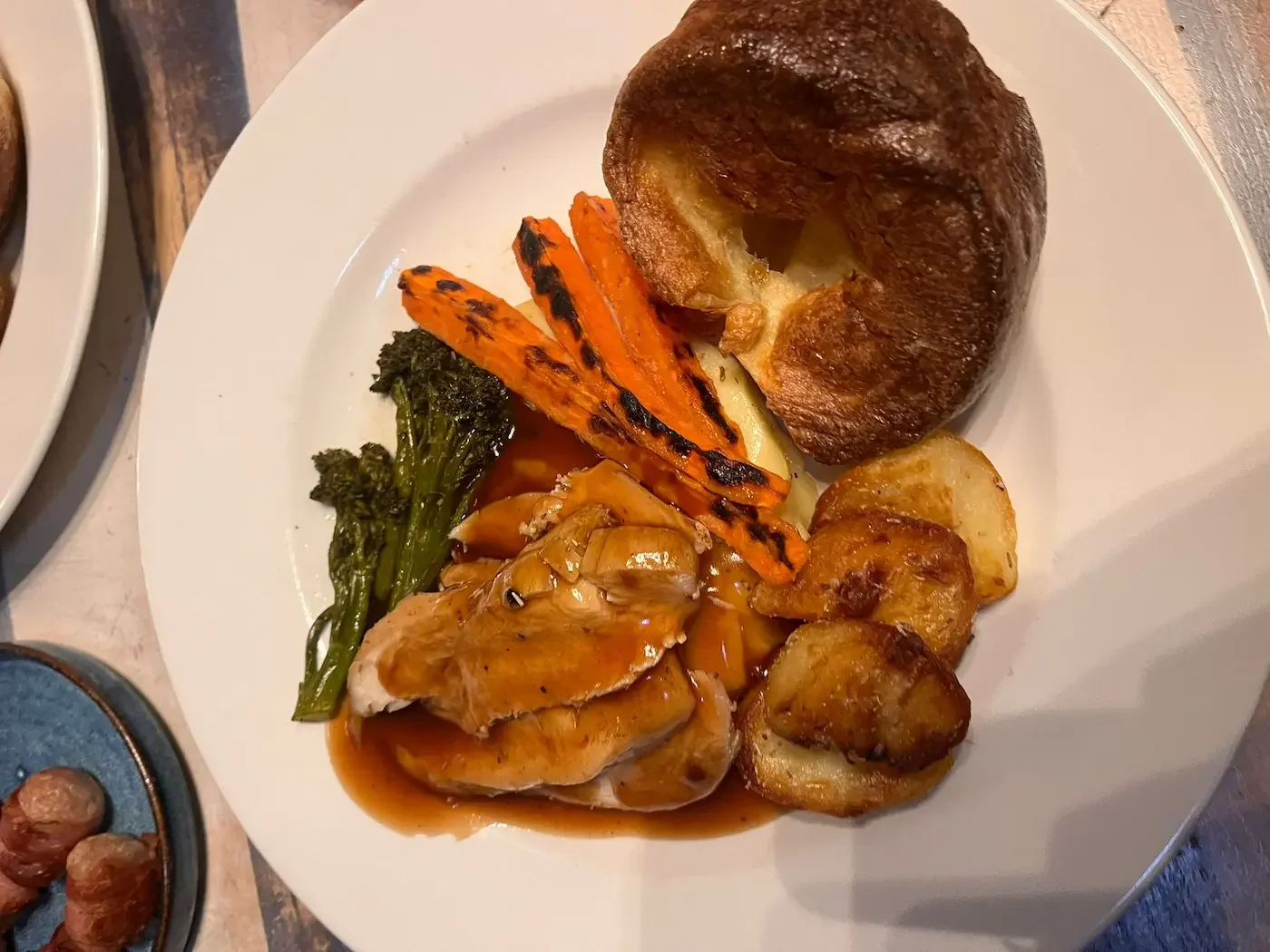 Plate with roasted chicken with gravy, grilled carrots, broccolini, roasted potatoes, and a bread roll.