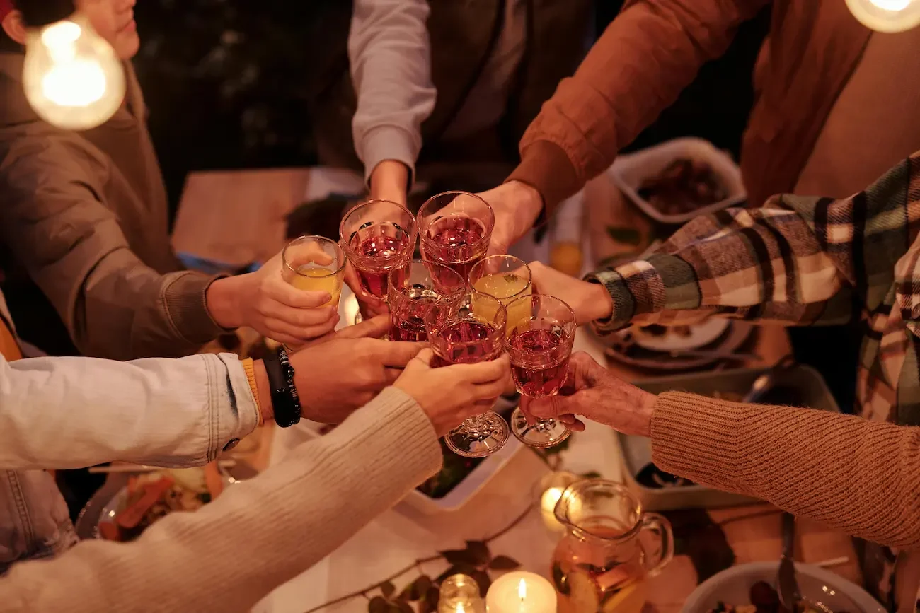 People raising glasses with pink and yellow drinks in a toast at a cozy dinner party.