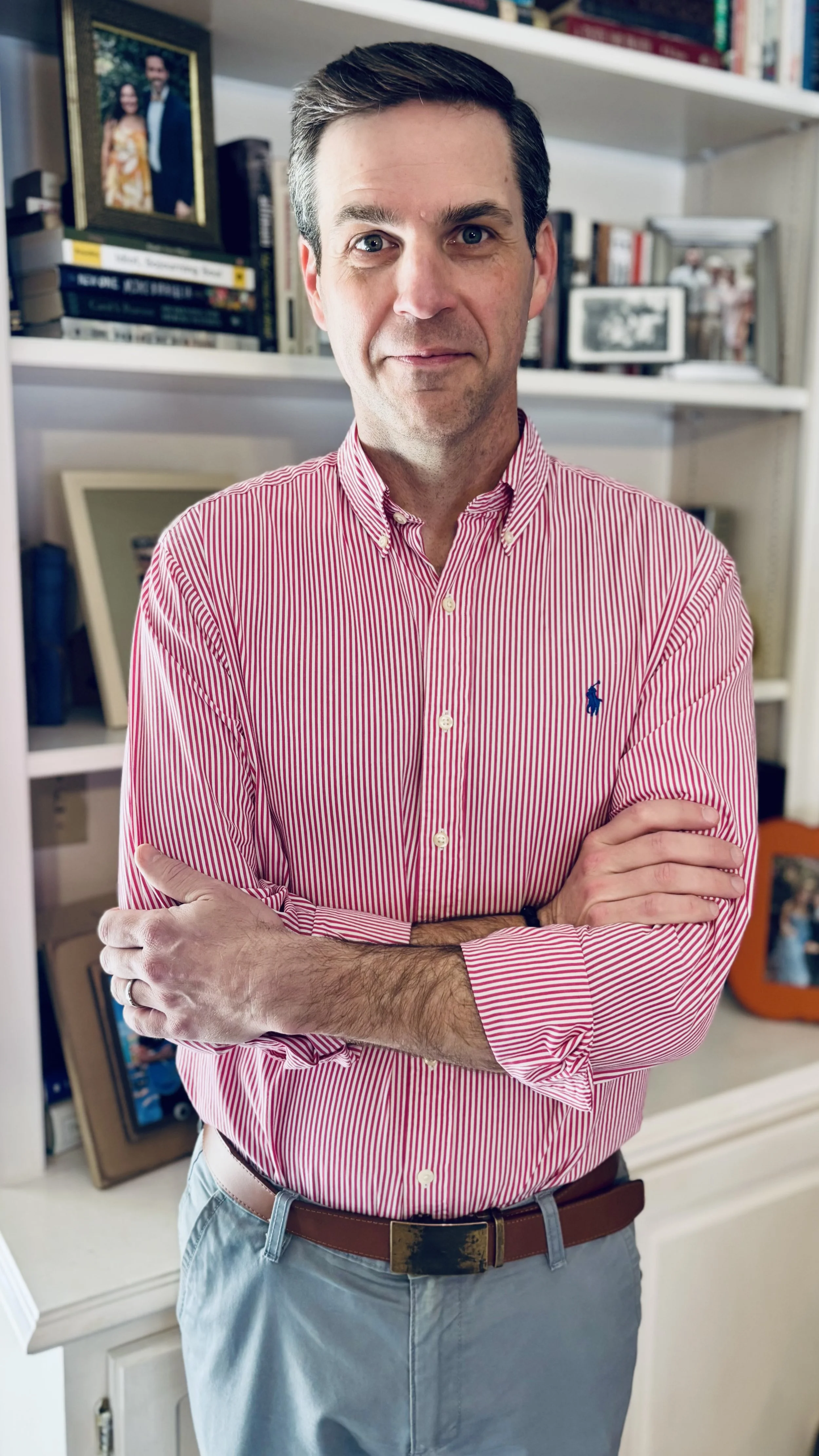 A picture of Micah Carver, standing in front of a bookshelf wearing a red and white striped button down.