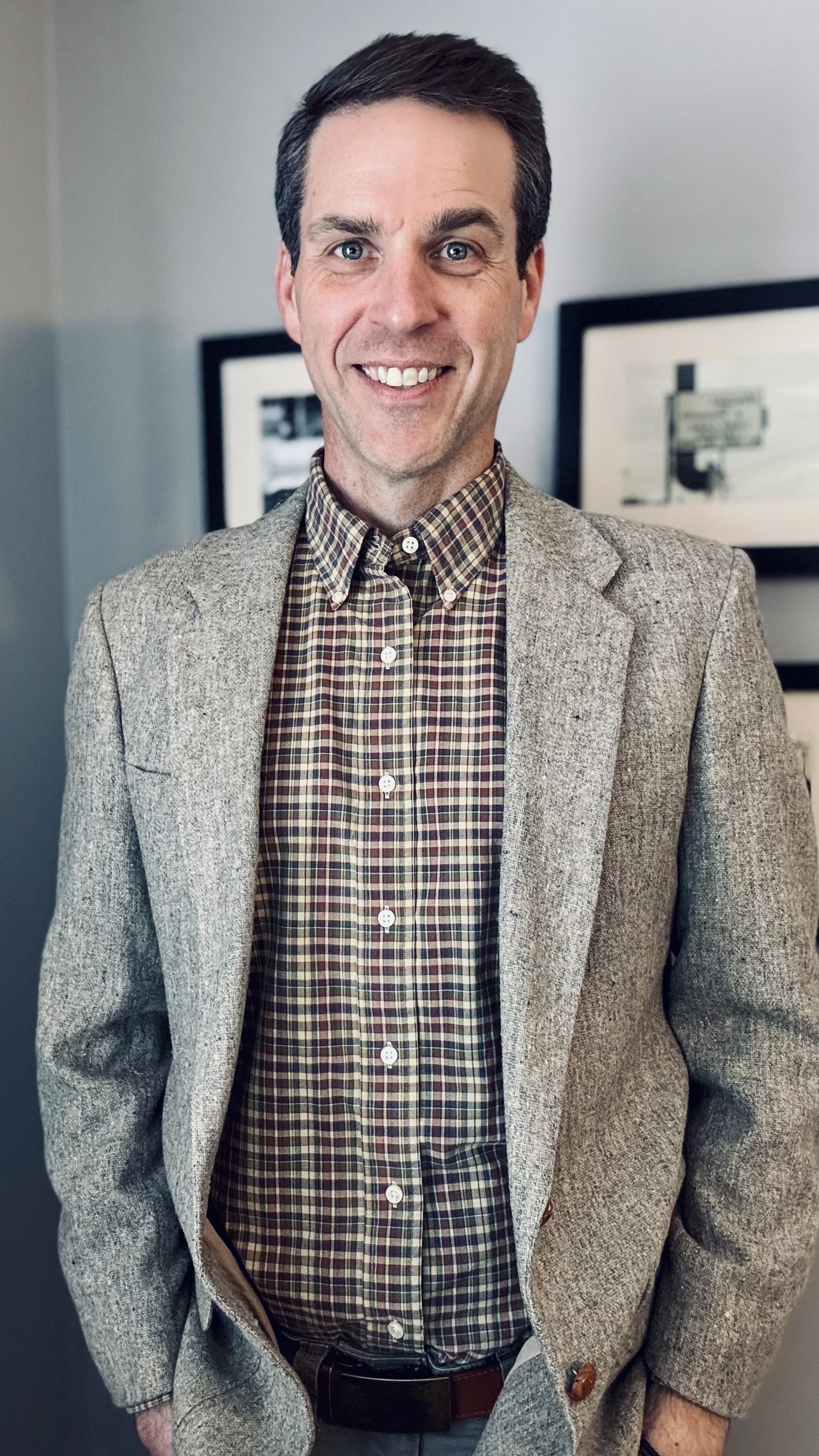 A picture of Micah Carver in a plaid button down shirt and tweed blazer.