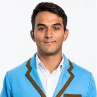 Portrait of a young man wearing a blue blazer with black and white trim, white shirt, and smiling against a white background.