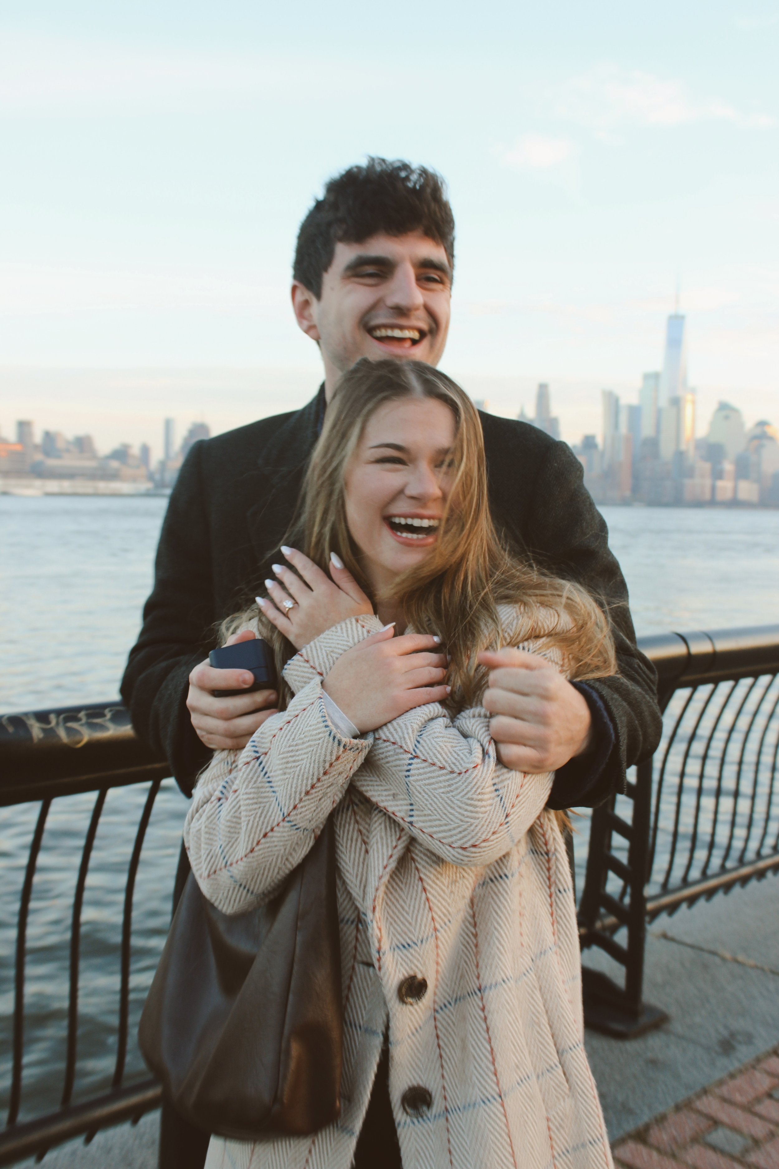 A happy young couple enjoying a moment by the river with the Manhattan skyline in the background, during sunset.