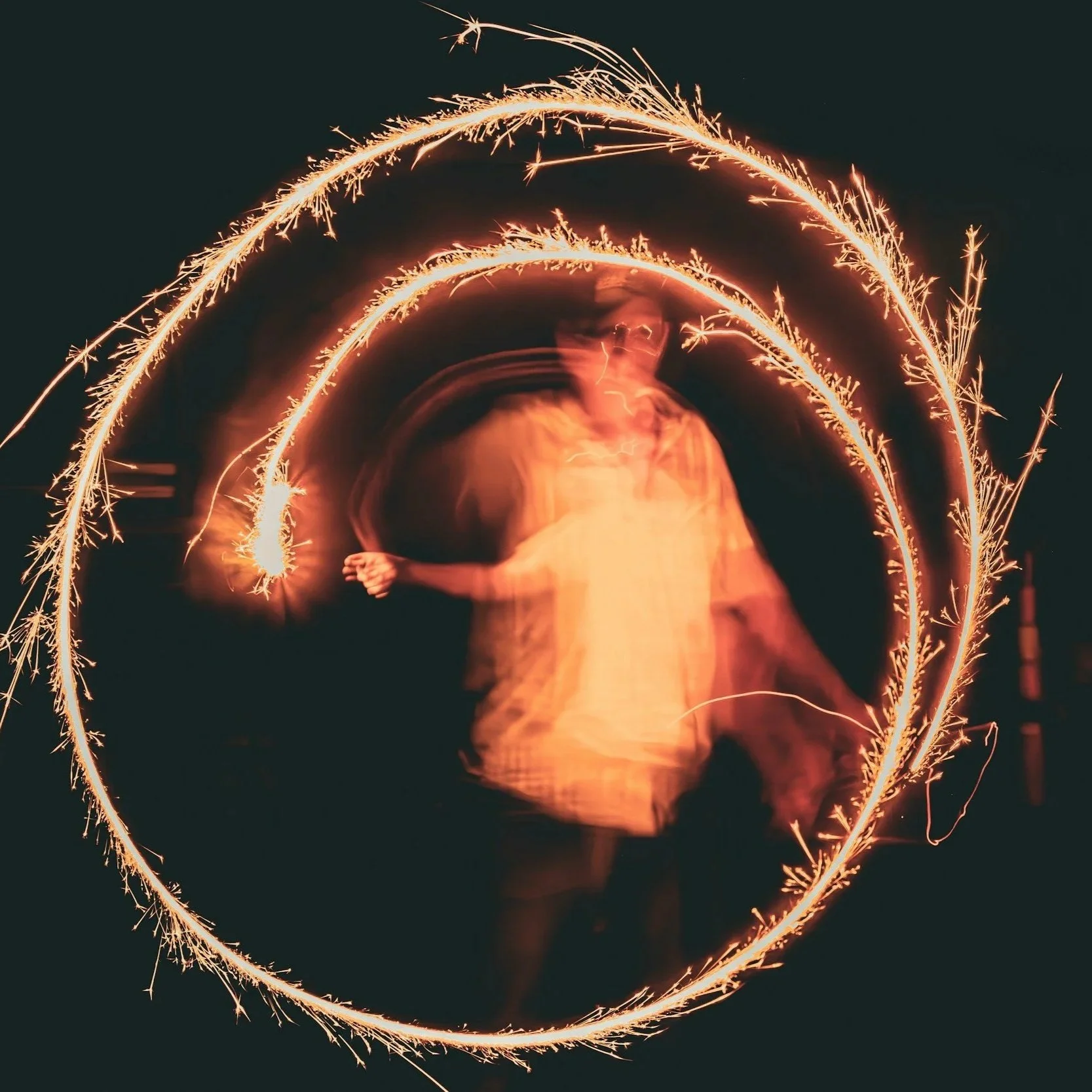 Person creating sparkler light trails in the shape of a heart against a dark background.