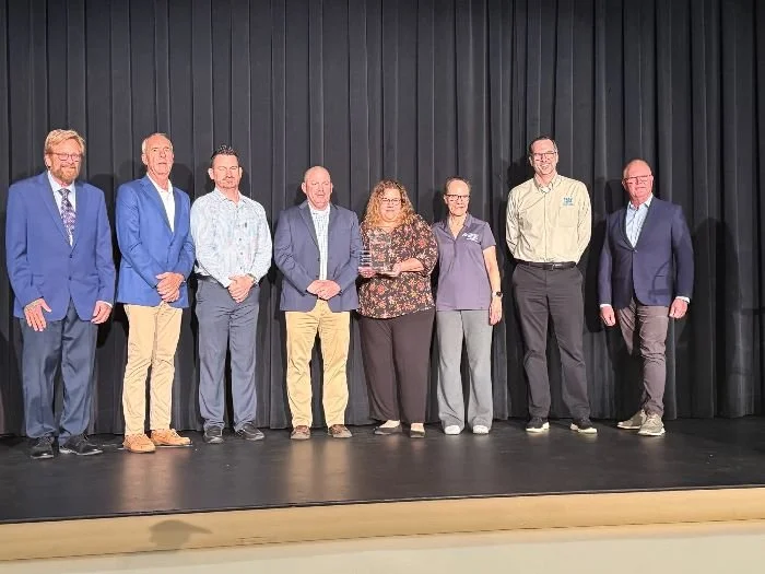 Eight conservation professionals standing on a stage in front of a black curtain, dressed in formal and business casual attire.