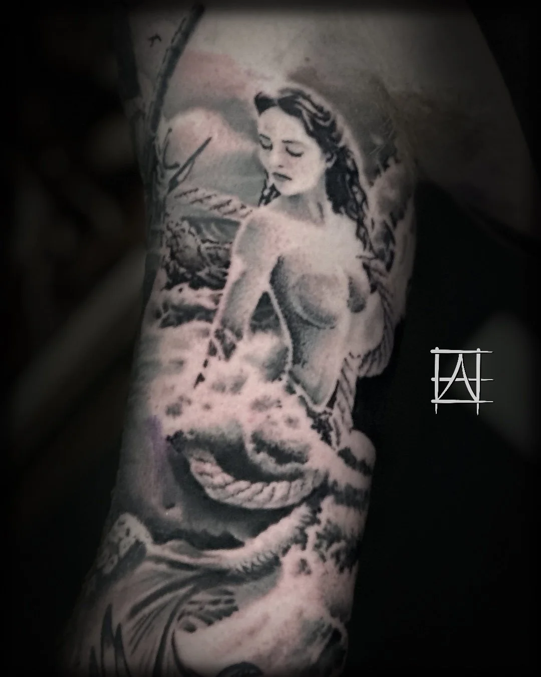 Black and gray tattoo of a woman with wet hair, holding a snake, with abstract background elements.