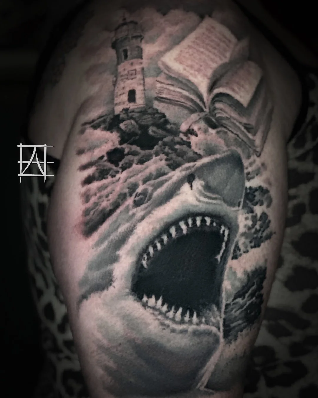 Tattoo of a lighthouse, shark, open book, and a wave in black and gray on skin.