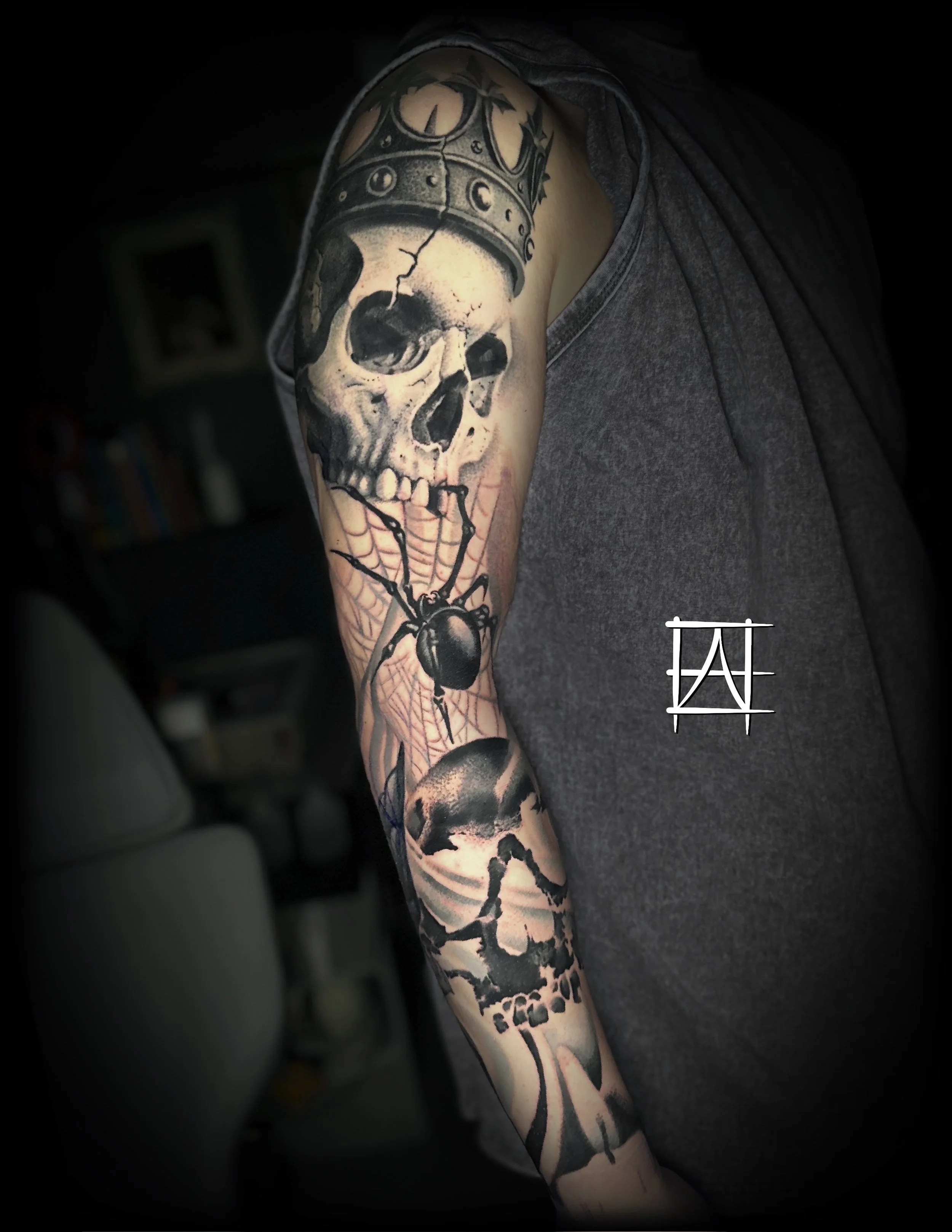 Tattooed arm featuring a skull with cracks, a crown, and a spider with a web covering part of the arm.