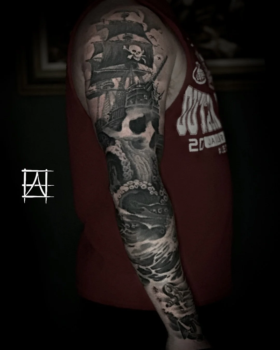 Tattoo sleeve featuring a pirate ship, a skull with waves, and ocean scenes on a person's arm.