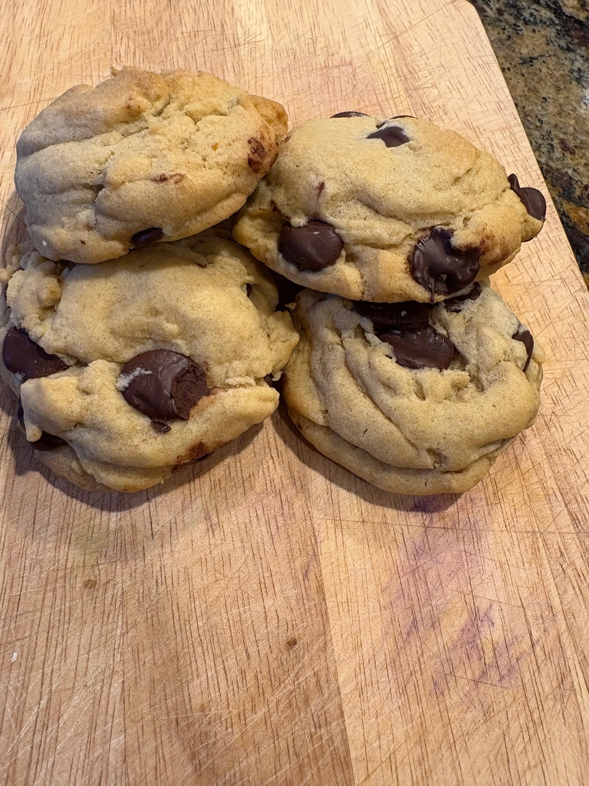 Four chocolate chip cookies on a wooden surface.