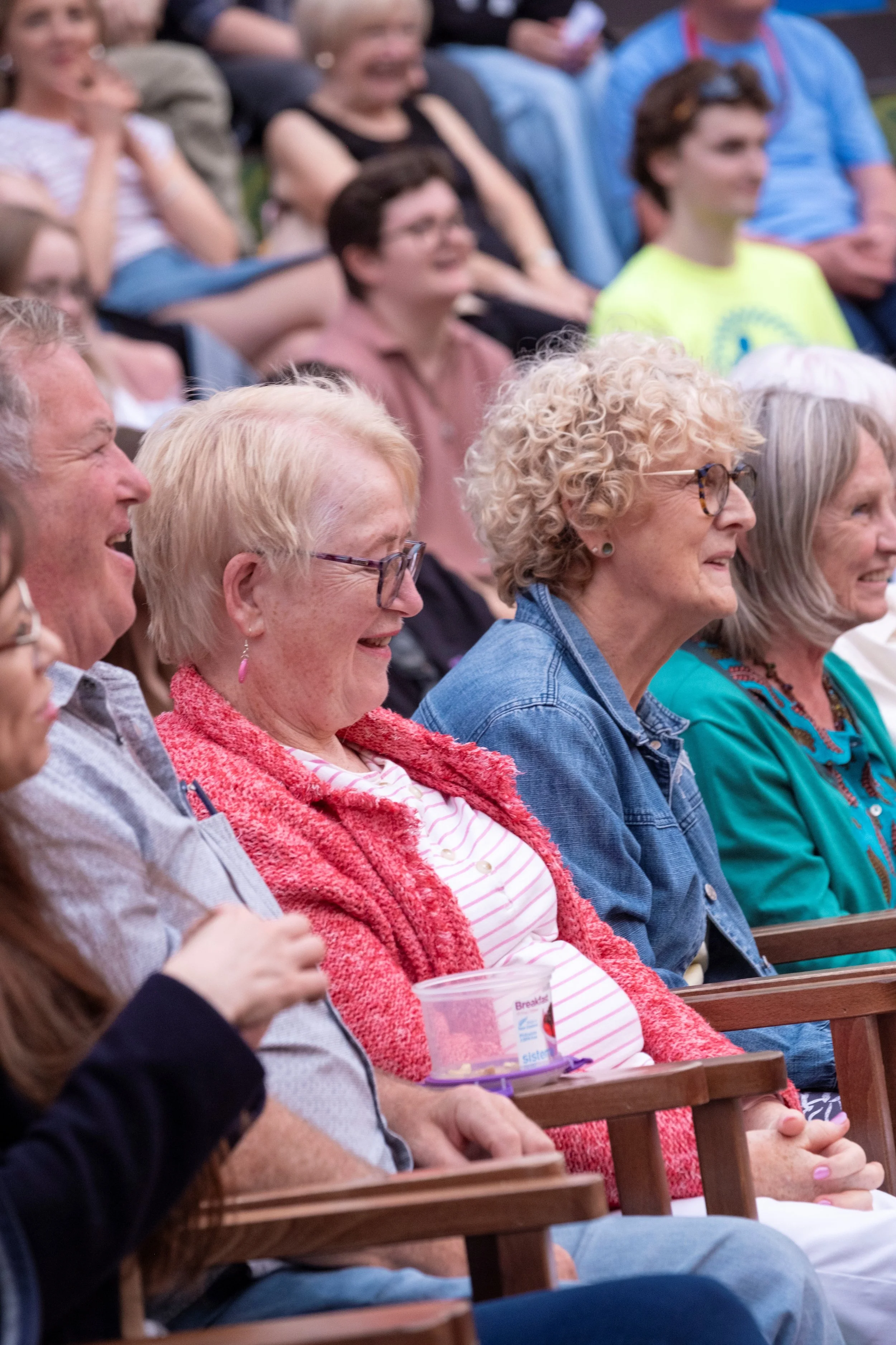 Audience seated and laughing during an outdoor event.