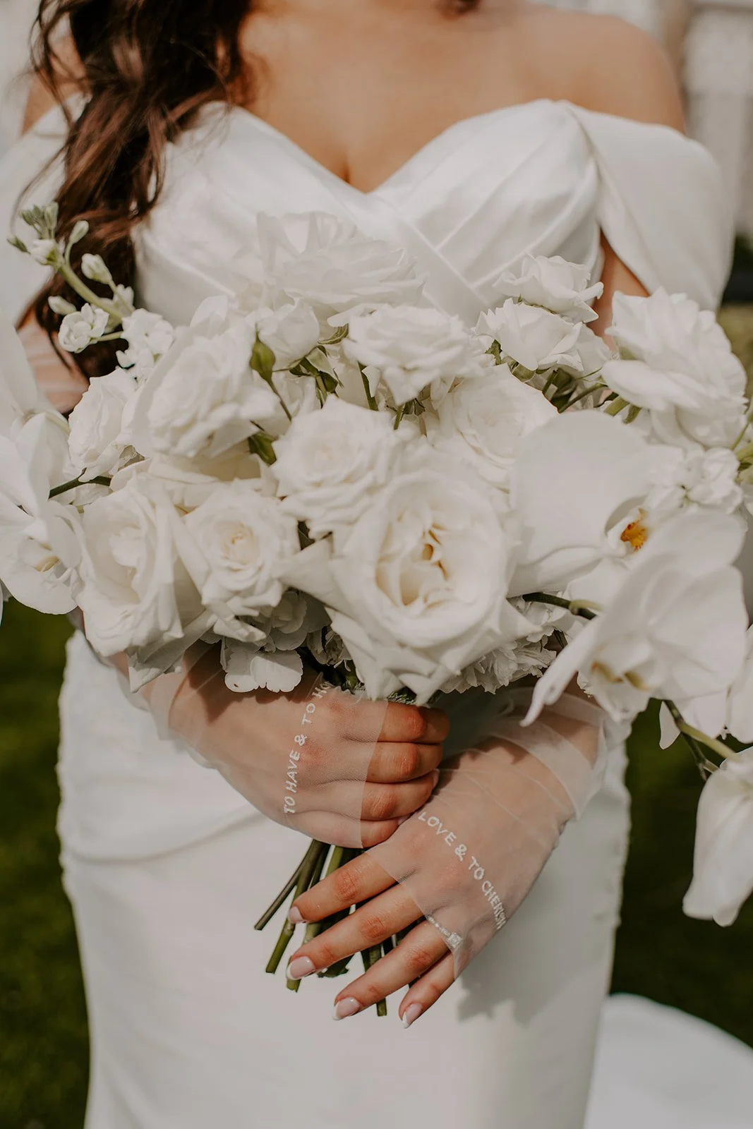 Woman in white dress holding a large bouquet of white flowers, including roses and orchids, outdoors