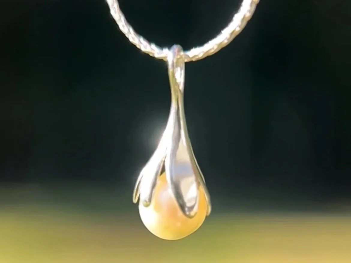 Close-up of a silver necklace and pendant with a tulip-style bail and a pearl hanging from a coiled chain.