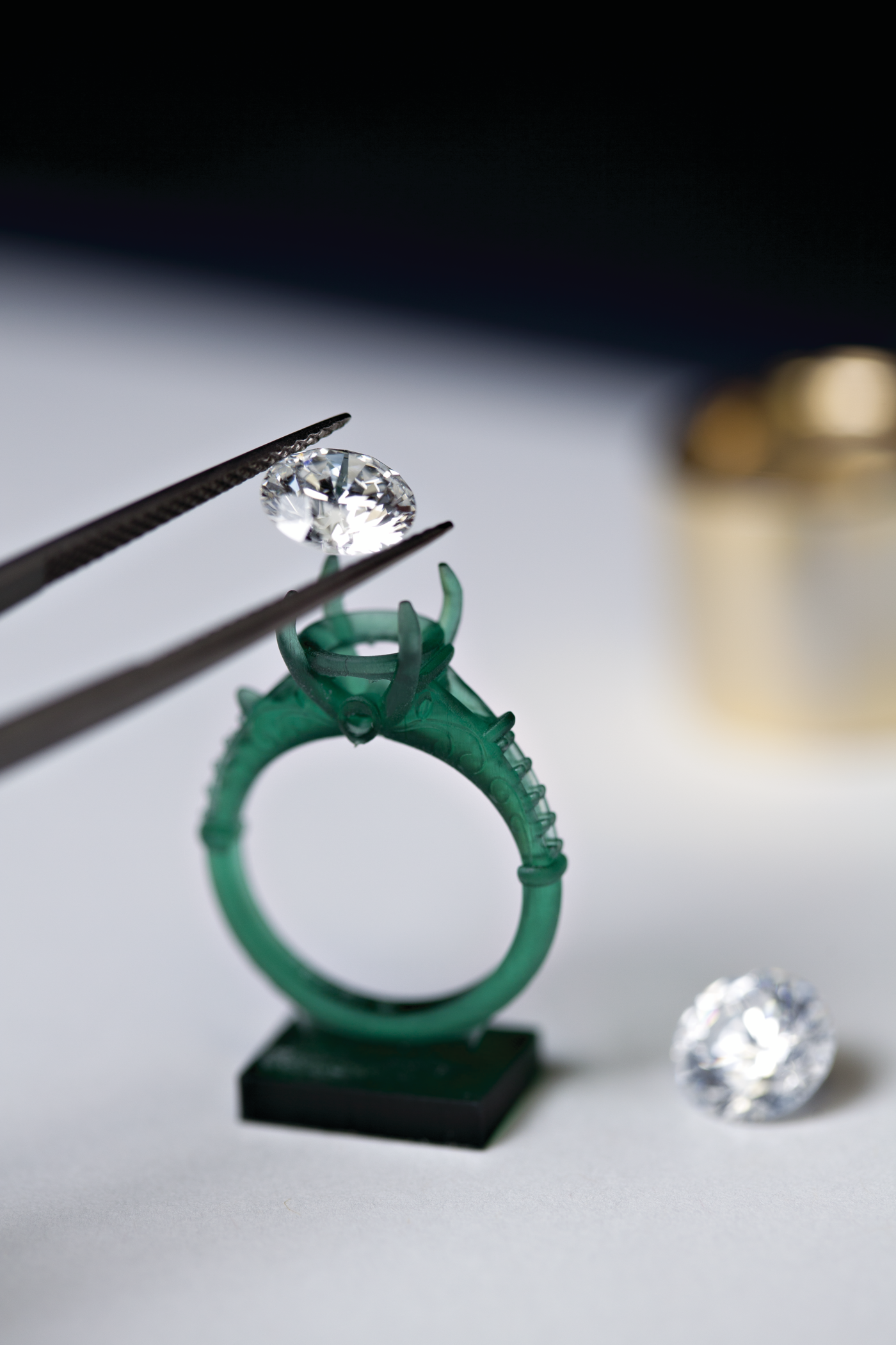 A diamond being held in tweezers above a wax casting of a ring during the custom design process.