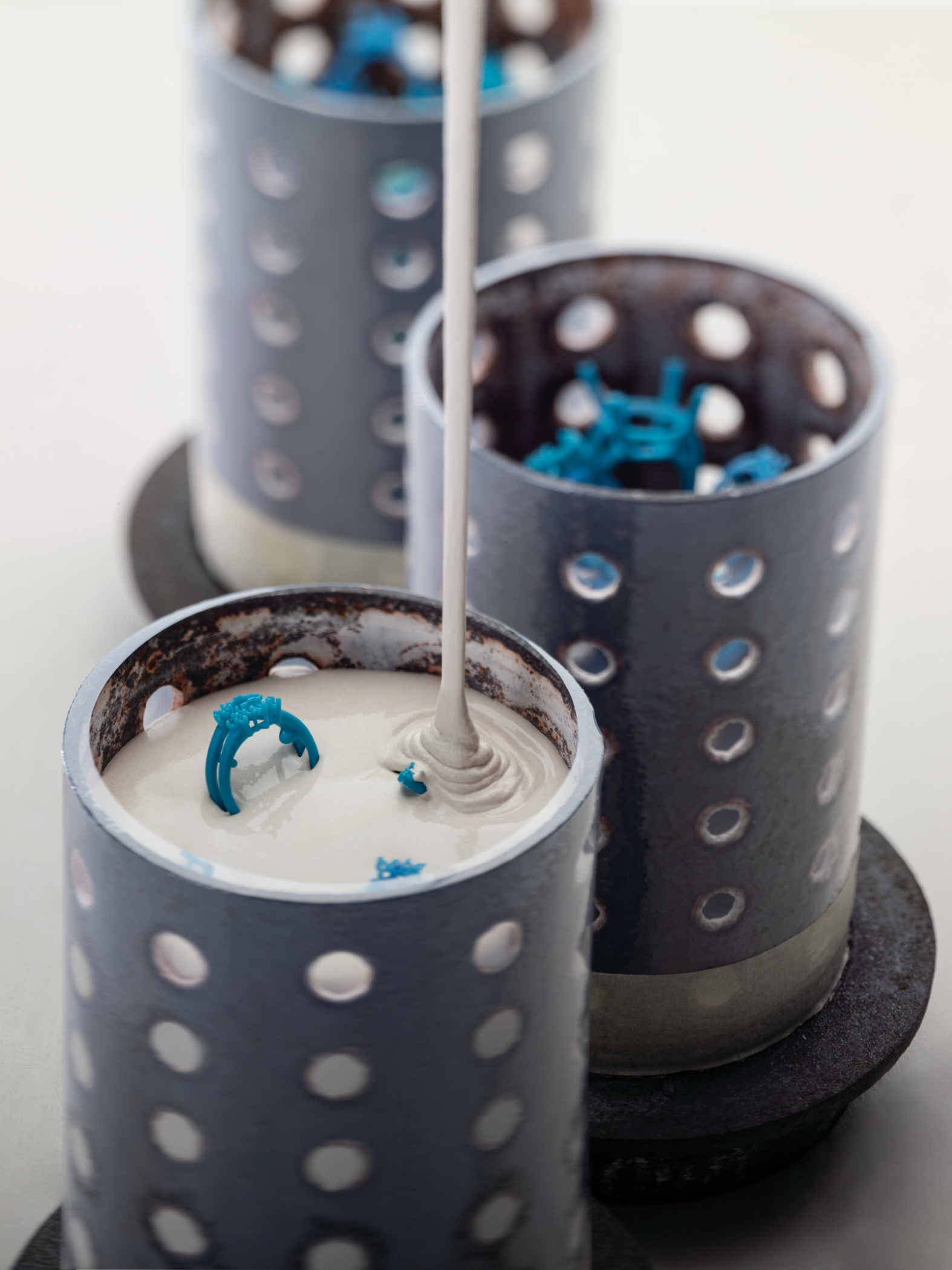 Three casting flasks with wax models of engagement rings being filled with plaster for casting.
