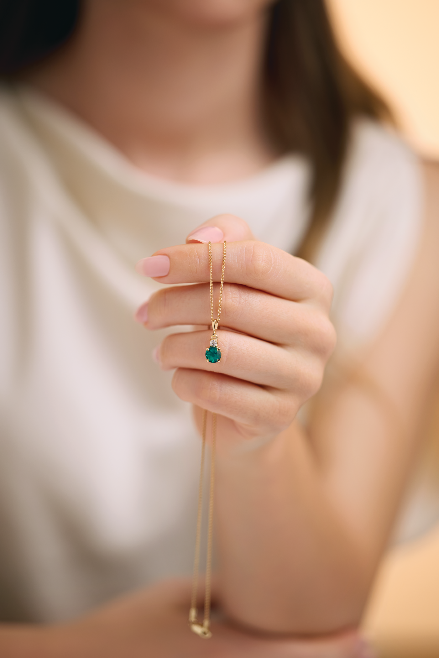 Close-up of a woman holding a gold necklace with a green gemstone pendant.